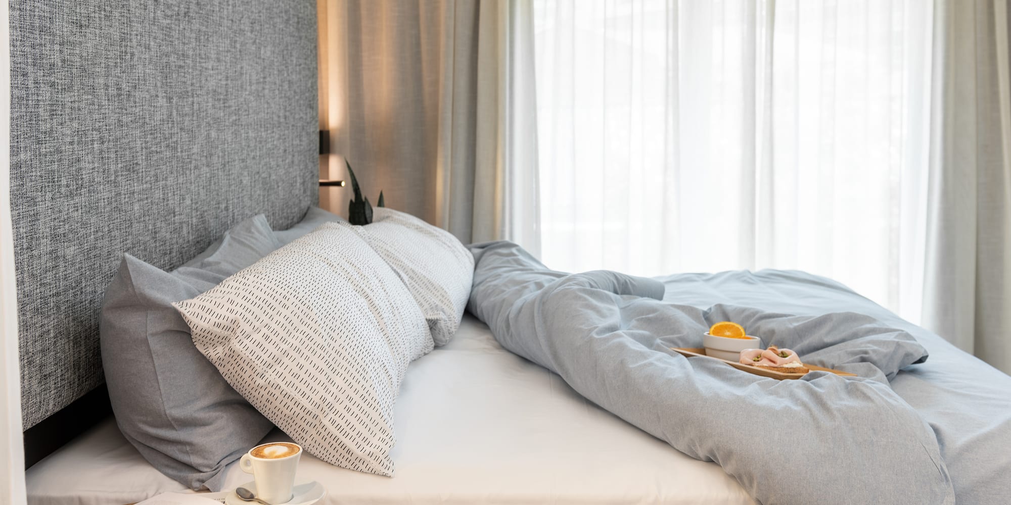 Cama moderna deshecha, desayuno en bandeja, café. Luz natural.
