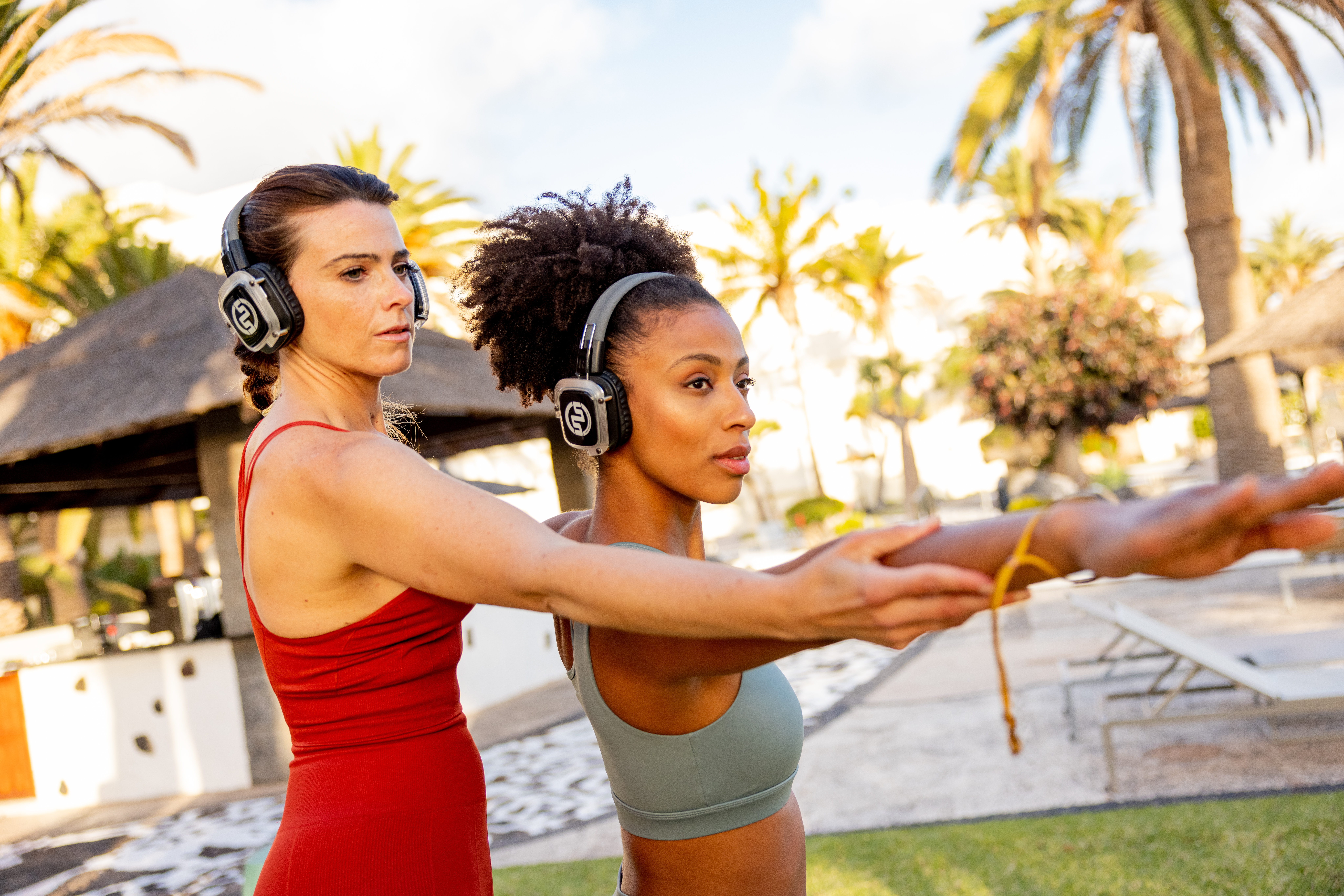 Diverse women stretching with headphones in a sunny tropical setting.