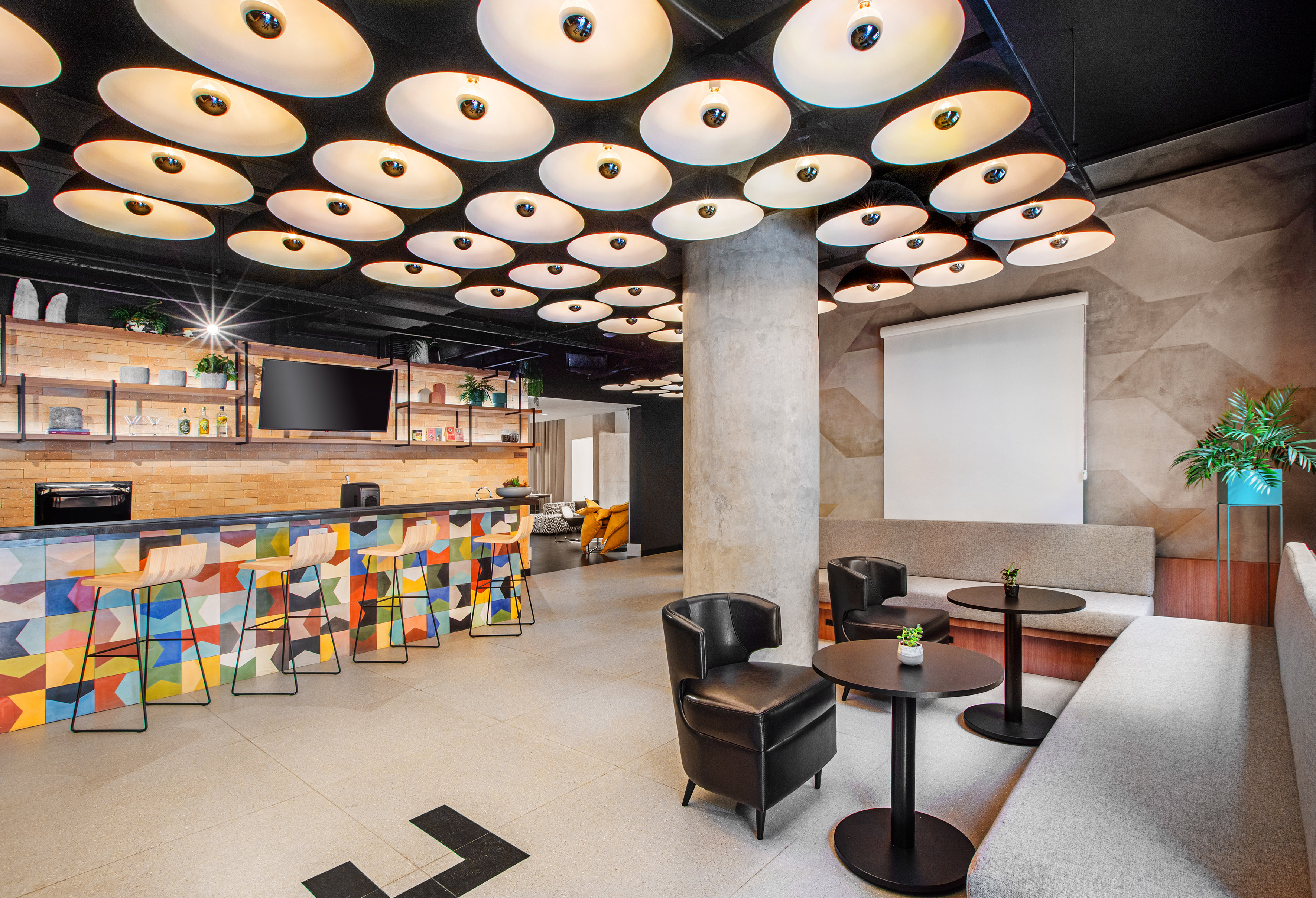 Modern bar lounge with colorful tiled counter, industrial lighting, and stylish seating.