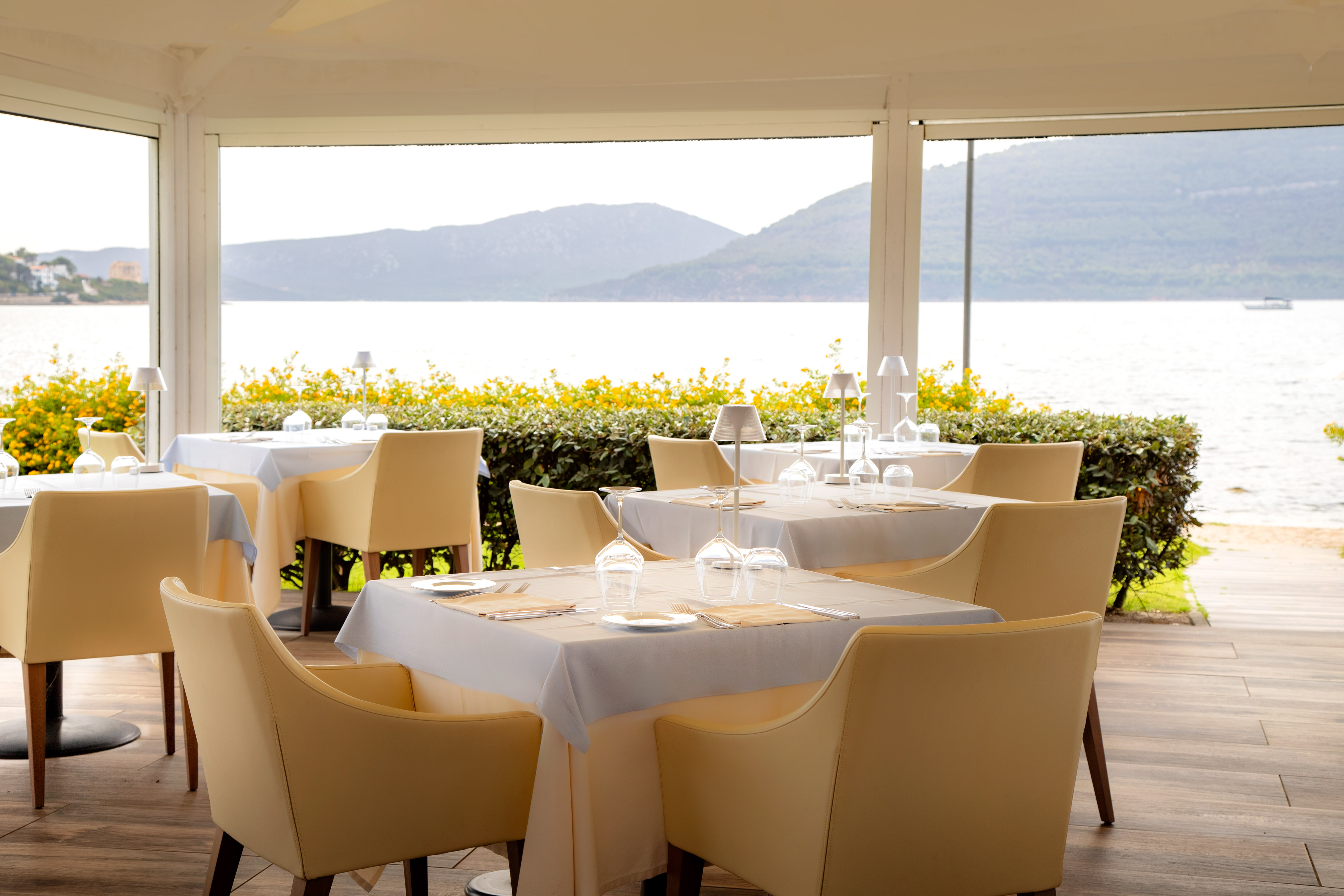 Waterfront restaurant patio with set tables, cream chairs, and sea view.