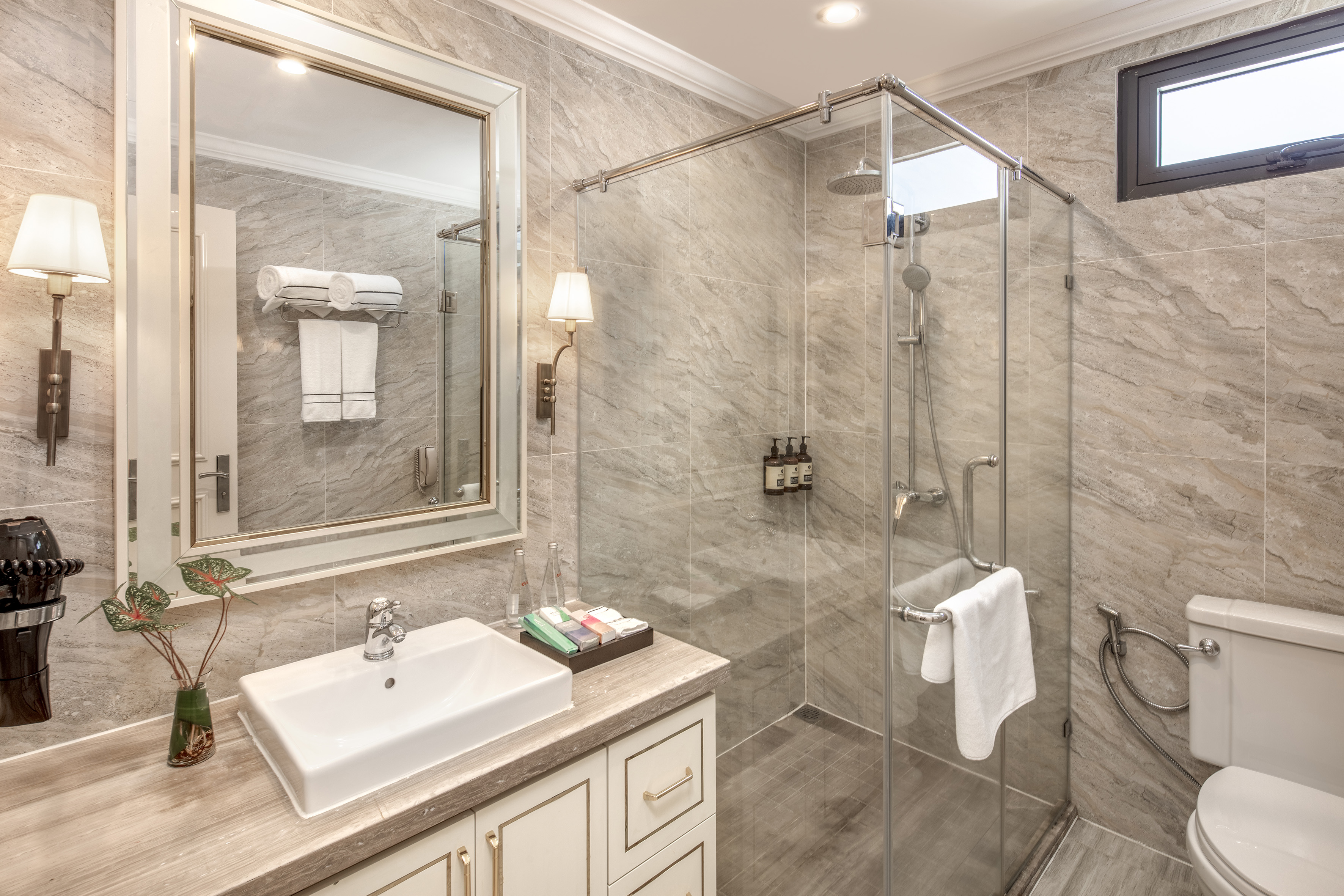 Modern tiled bathroom with large mirror, vanity, and glass shower.