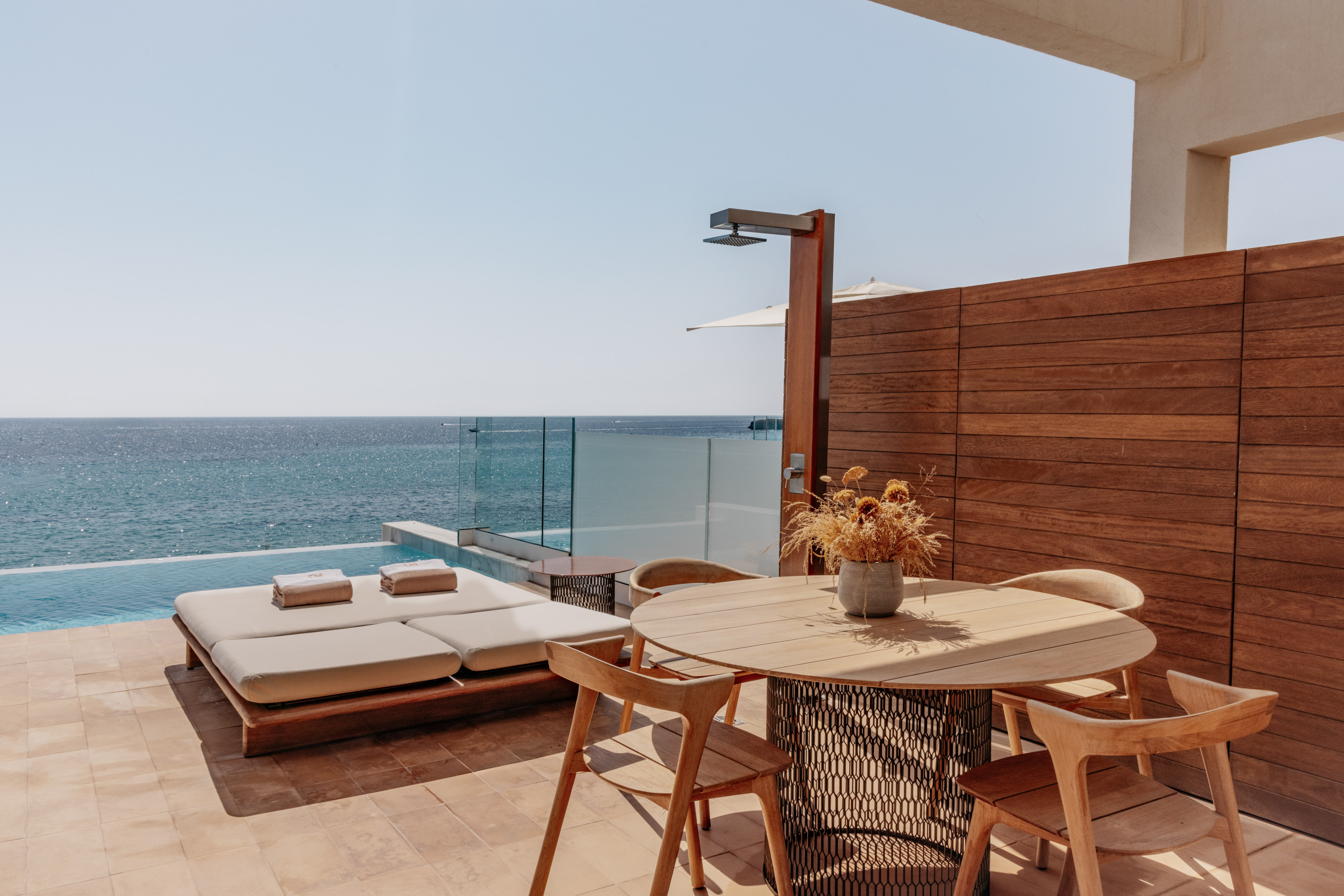 Luxury oceanfront patio with private infinity pool, sun lounger, dining area.