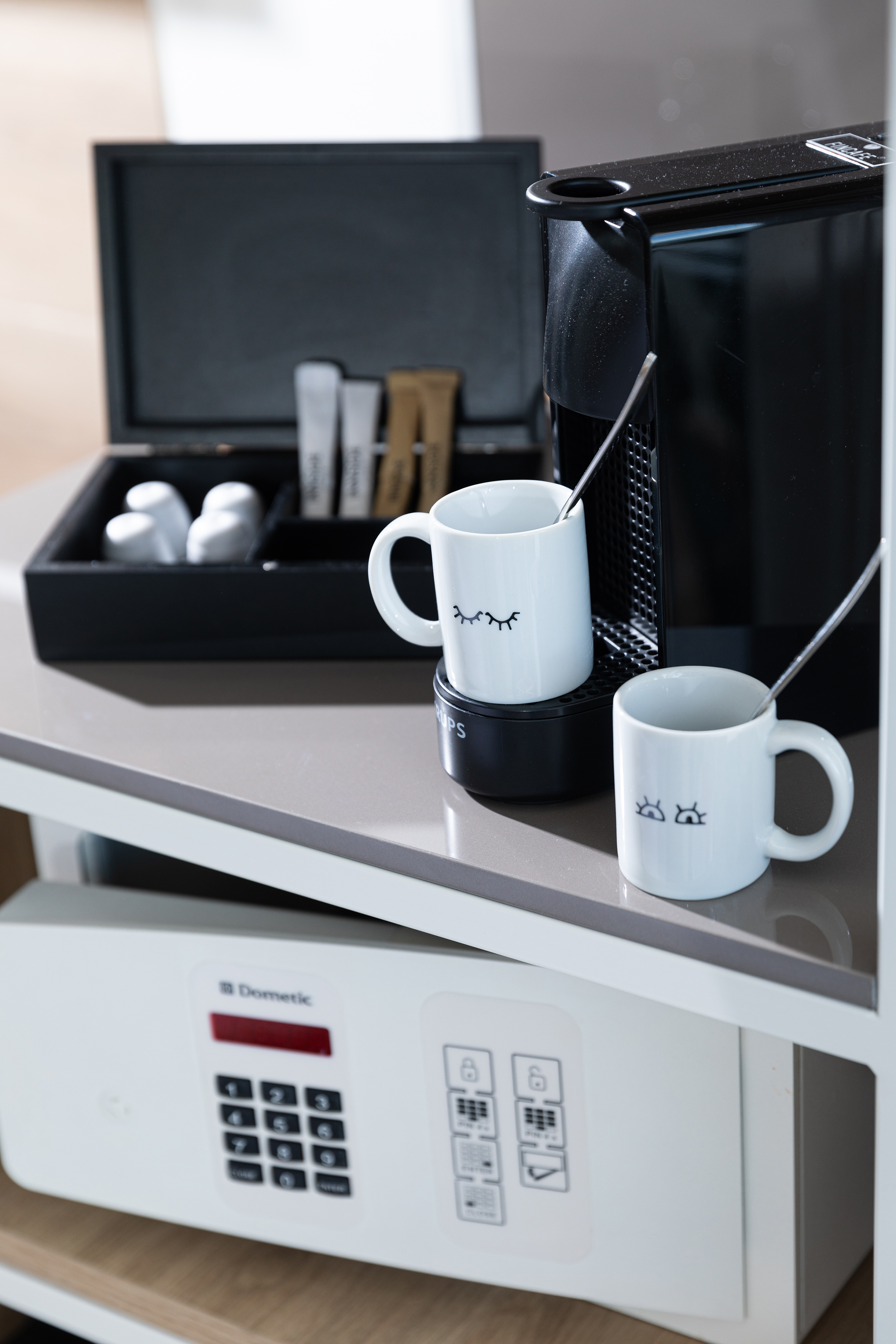 Hotel coffee station with Nespresso machine, mugs, sugar, and Dometic safe.