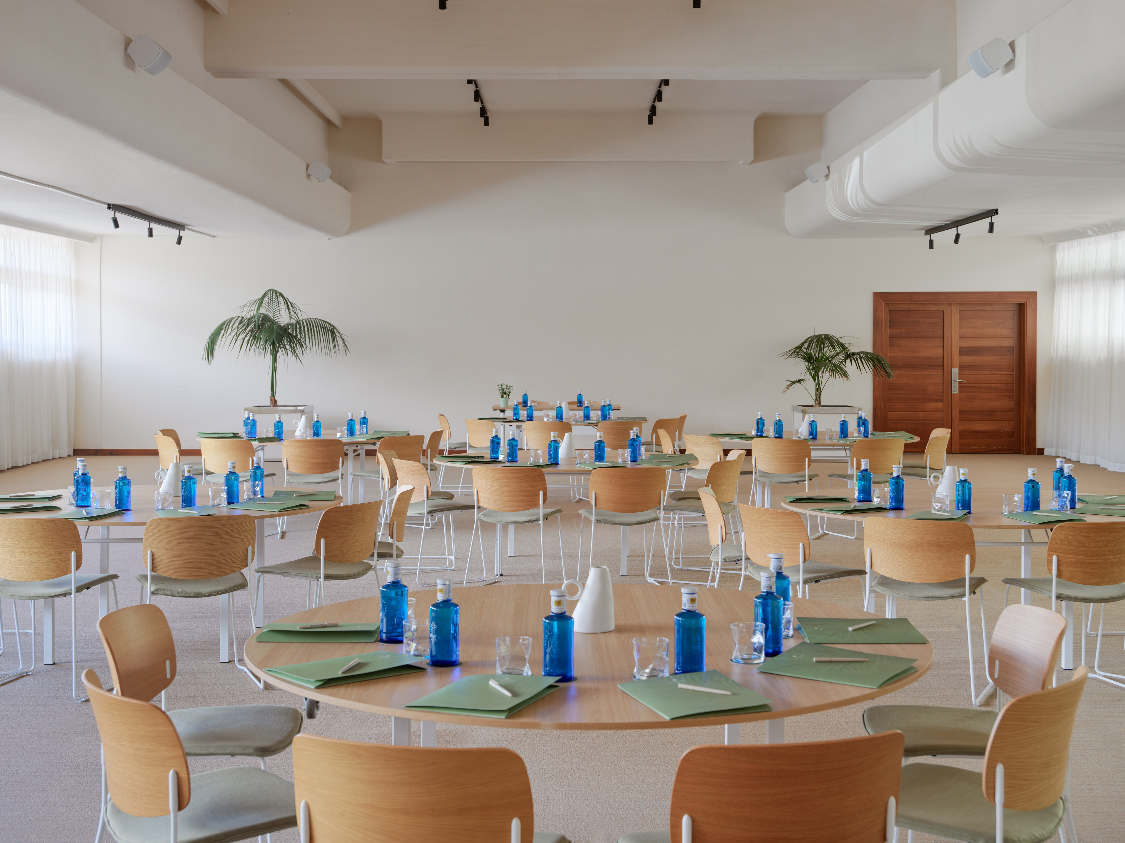 Modern conference room with round tables, wood chairs, blue water bottles.