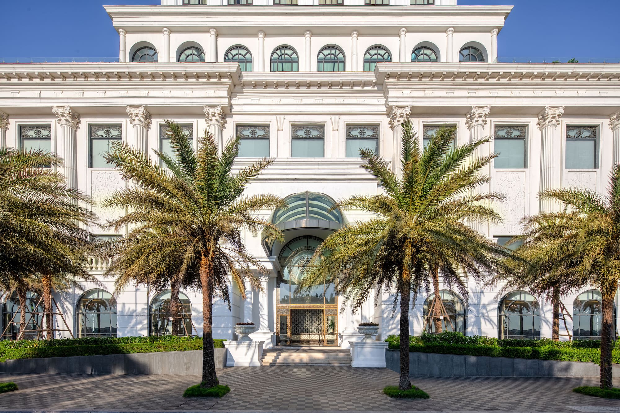 Grand white neoclassical building facade with palm trees and glass entrance.