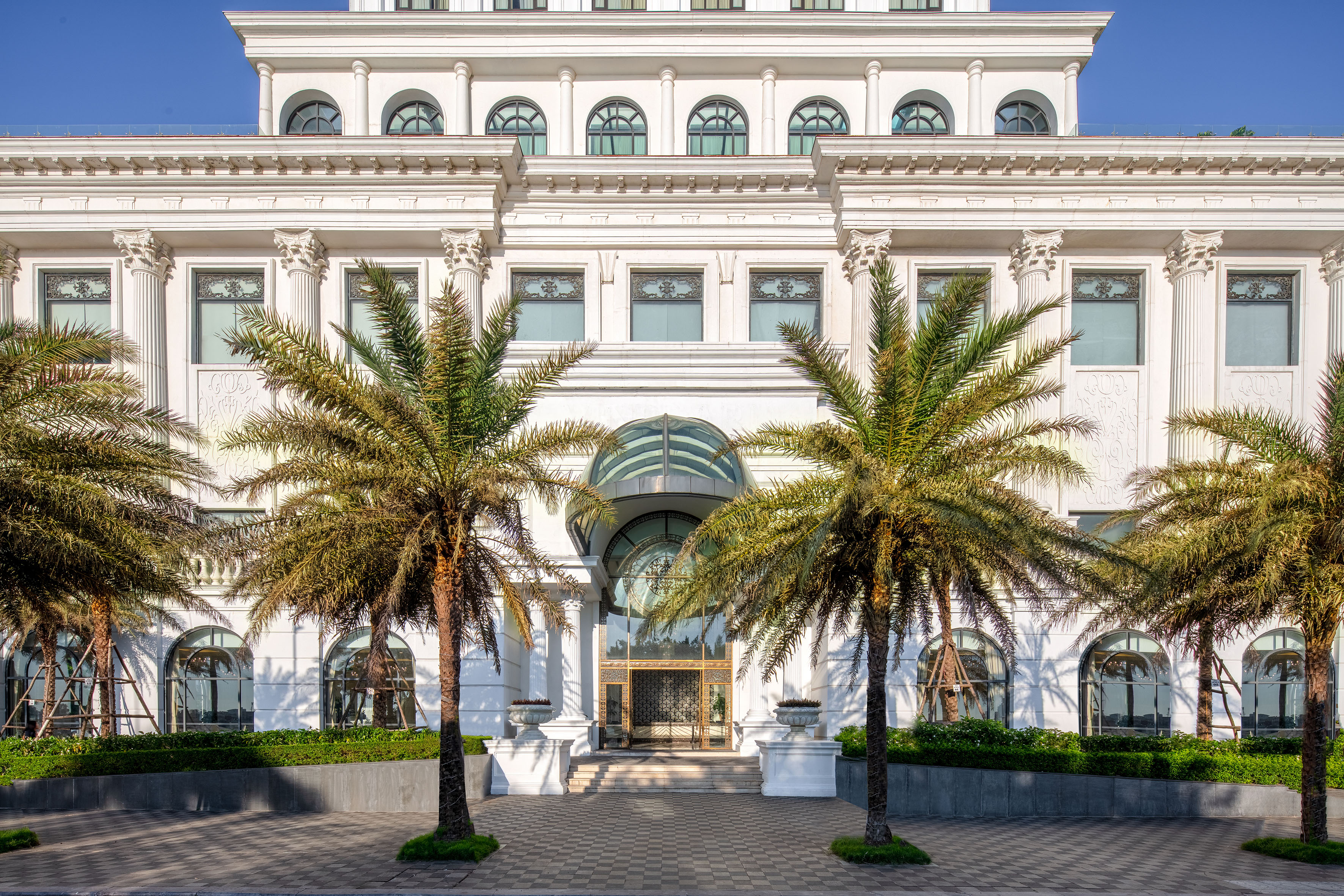 Grand white neoclassical building facade with palm trees and glass entrance.