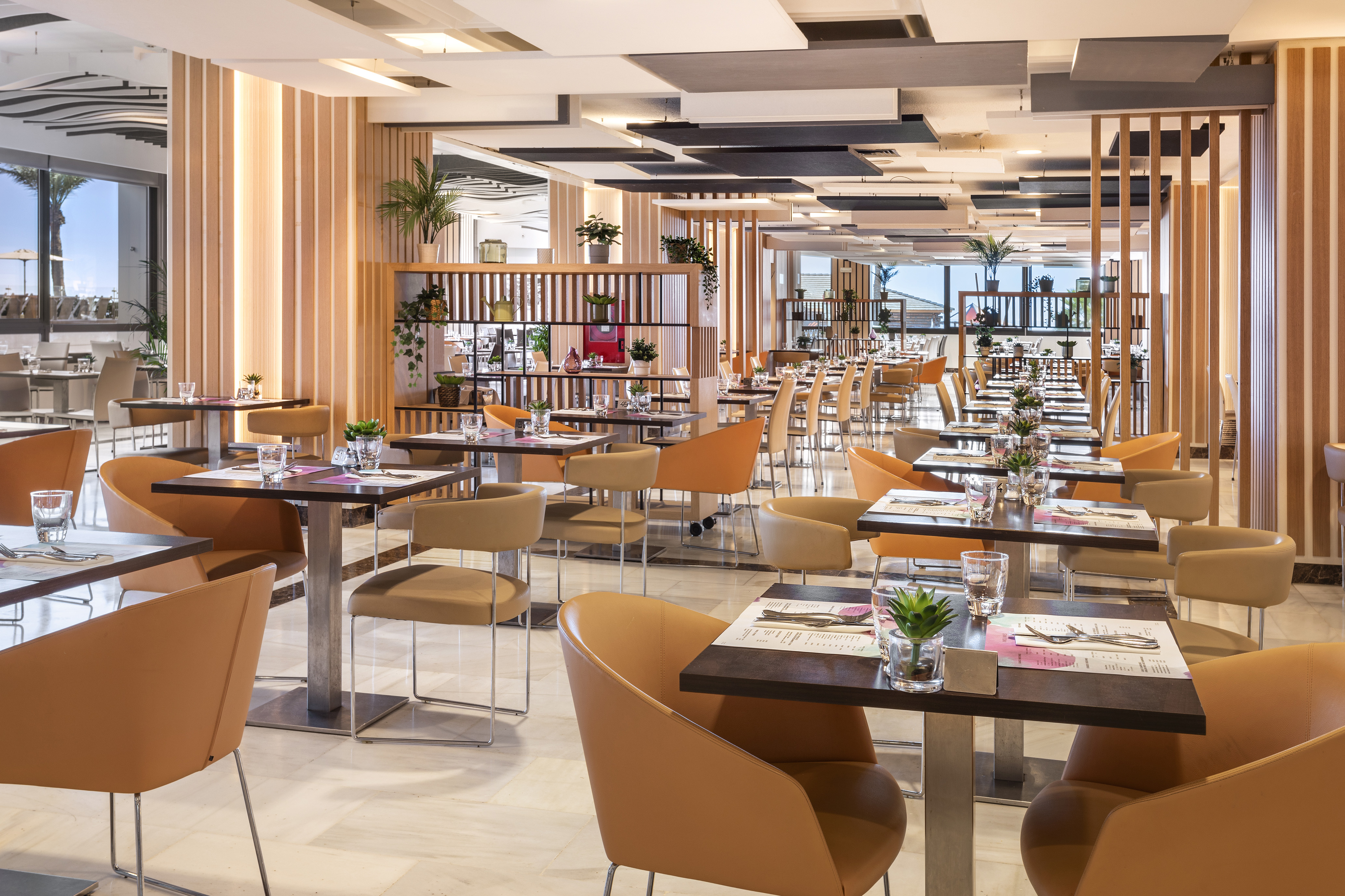 Modern restaurant dining area with orange chairs, wooden screens, and set tables.