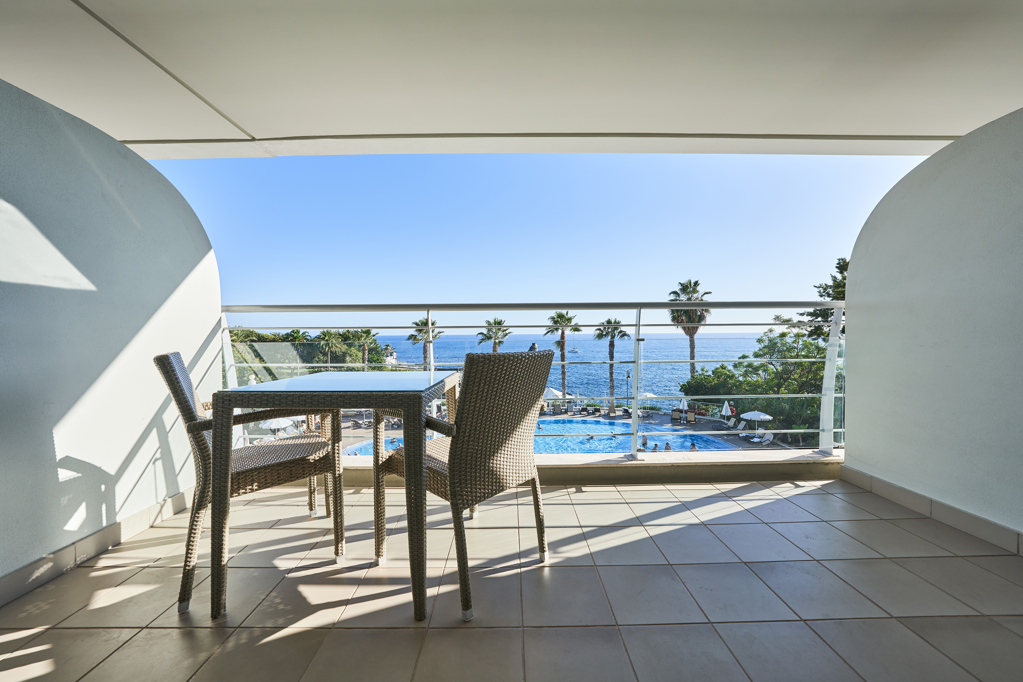 Hotel balcony with ocean view, swimming pool, and palm trees.
