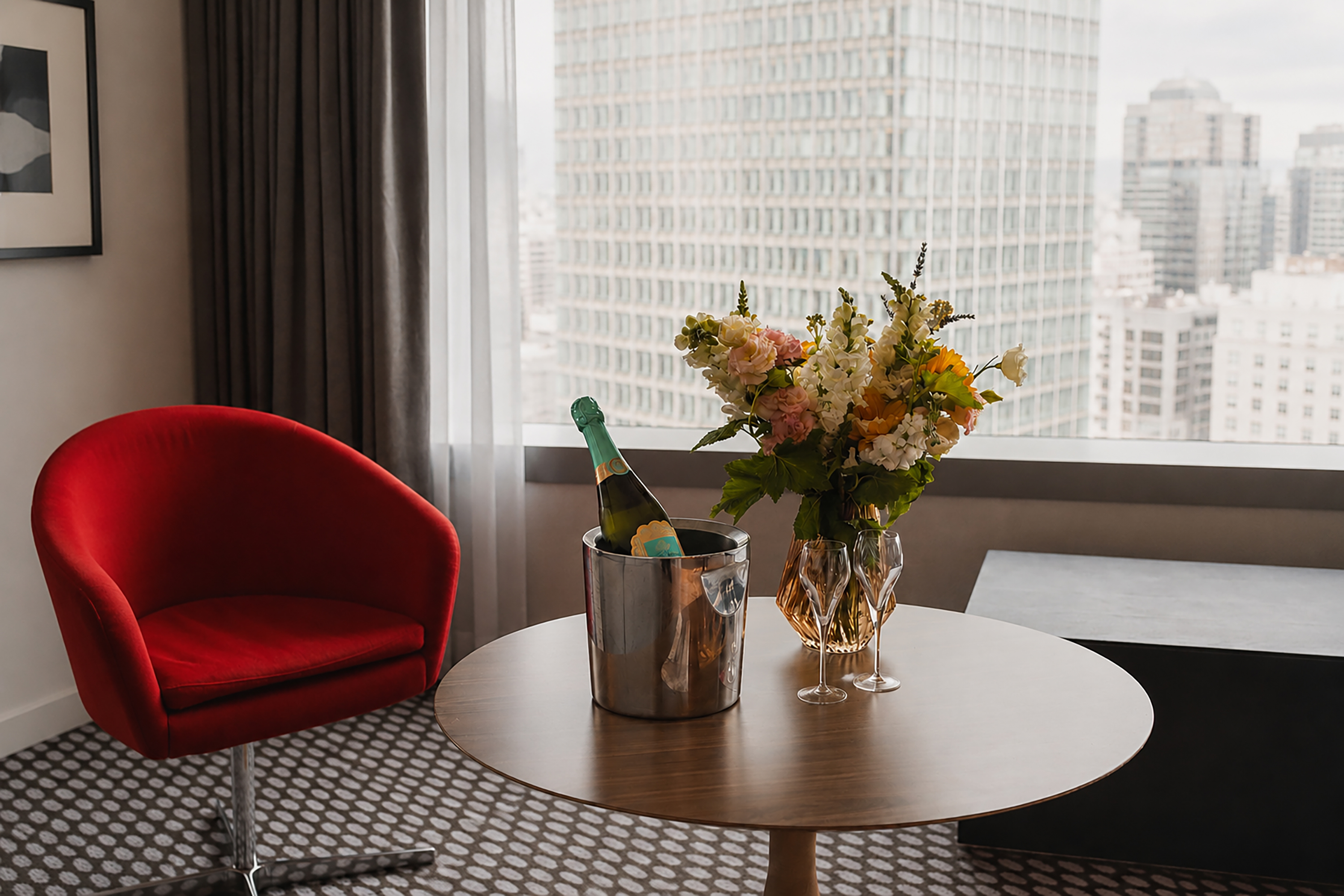 Luxury hotel room with city skyline view, champagne, and flowers.
