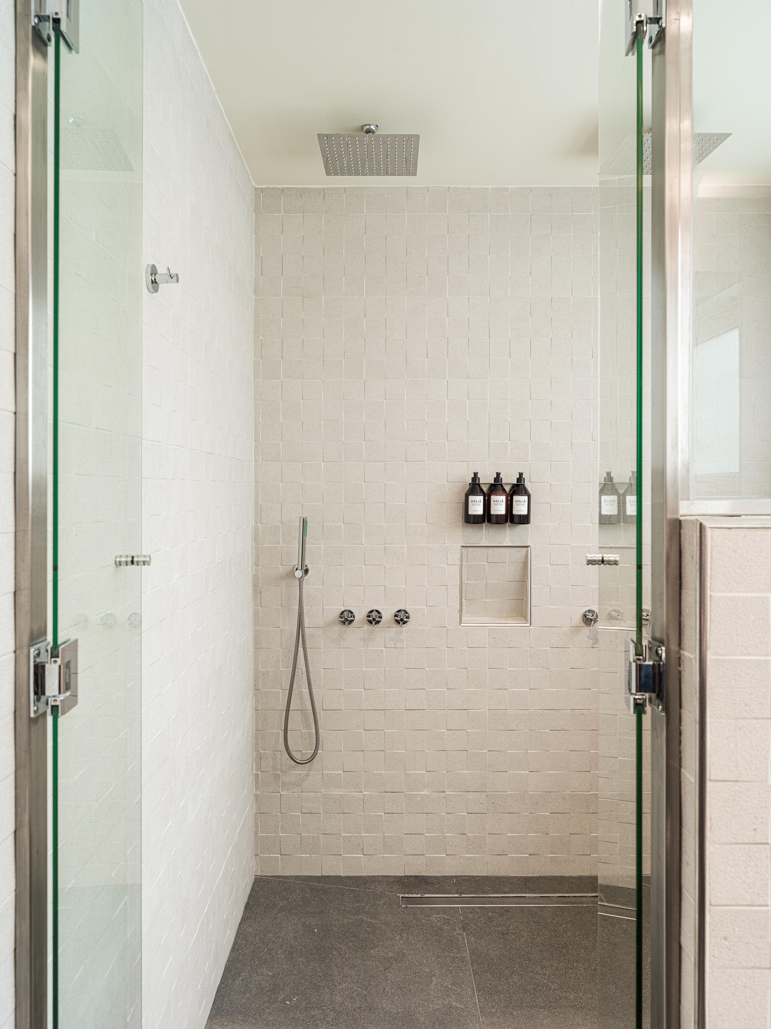 Modern walk-in shower with white textured tiles, glass doors, and rain shower head.