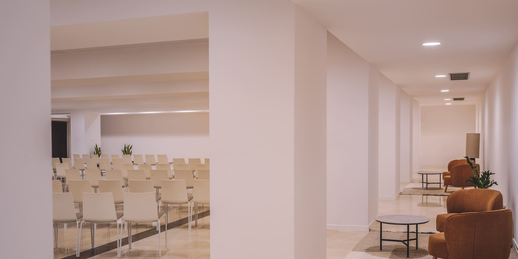 Modern conference and lounge space with white chairs and brown armchairs.