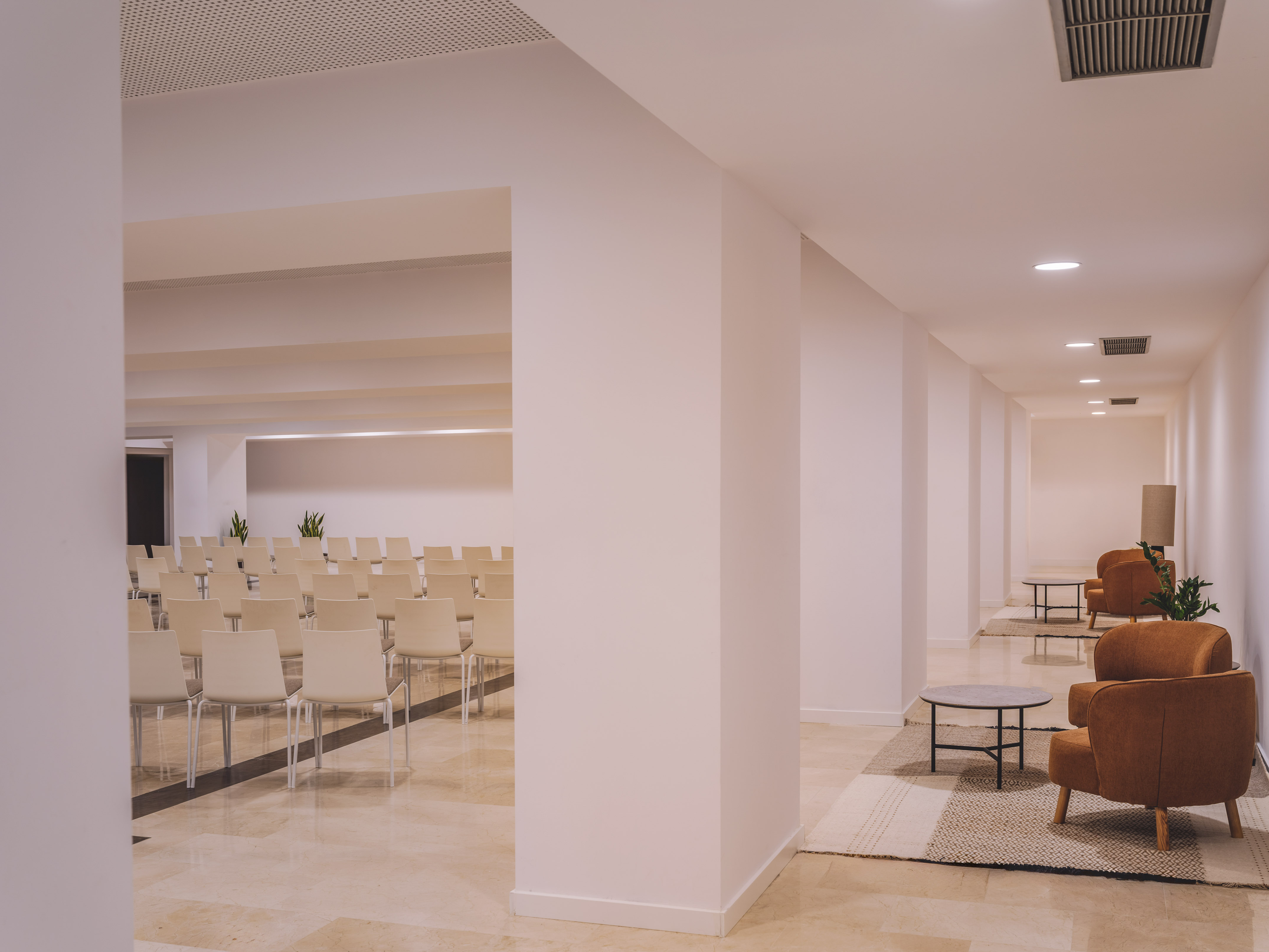 Modern conference and lounge space with white chairs and brown armchairs.