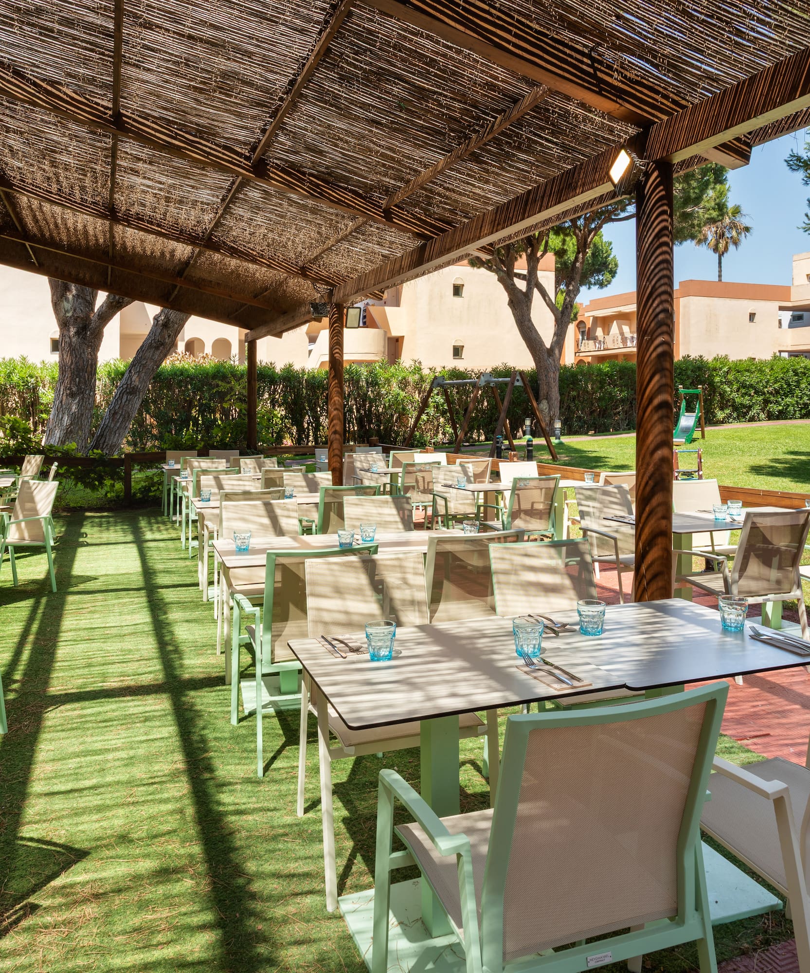 Shaded resort outdoor dining area, tables, chairs, and kids' playground.