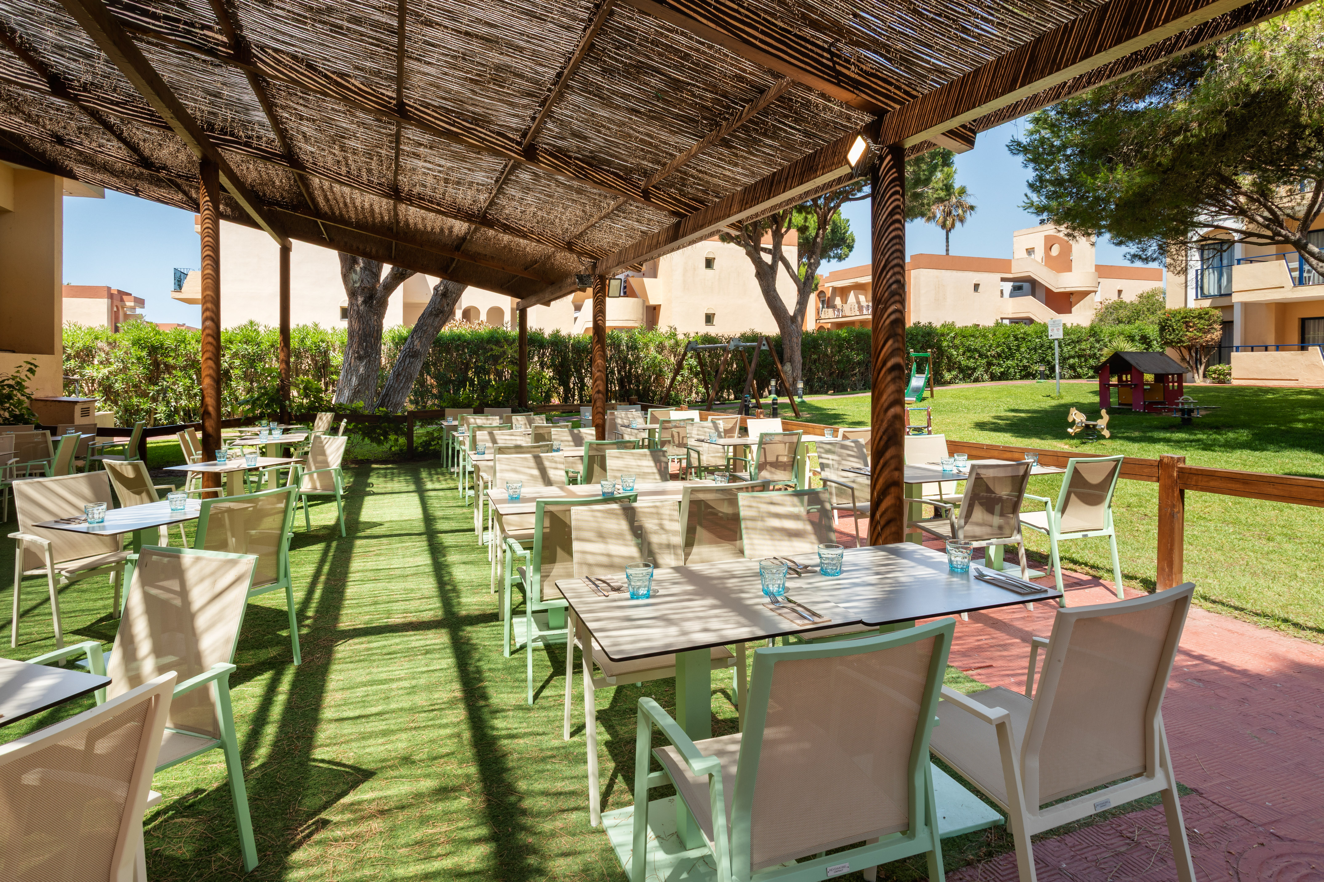 Shaded resort outdoor dining area, tables, chairs, and kids' playground.