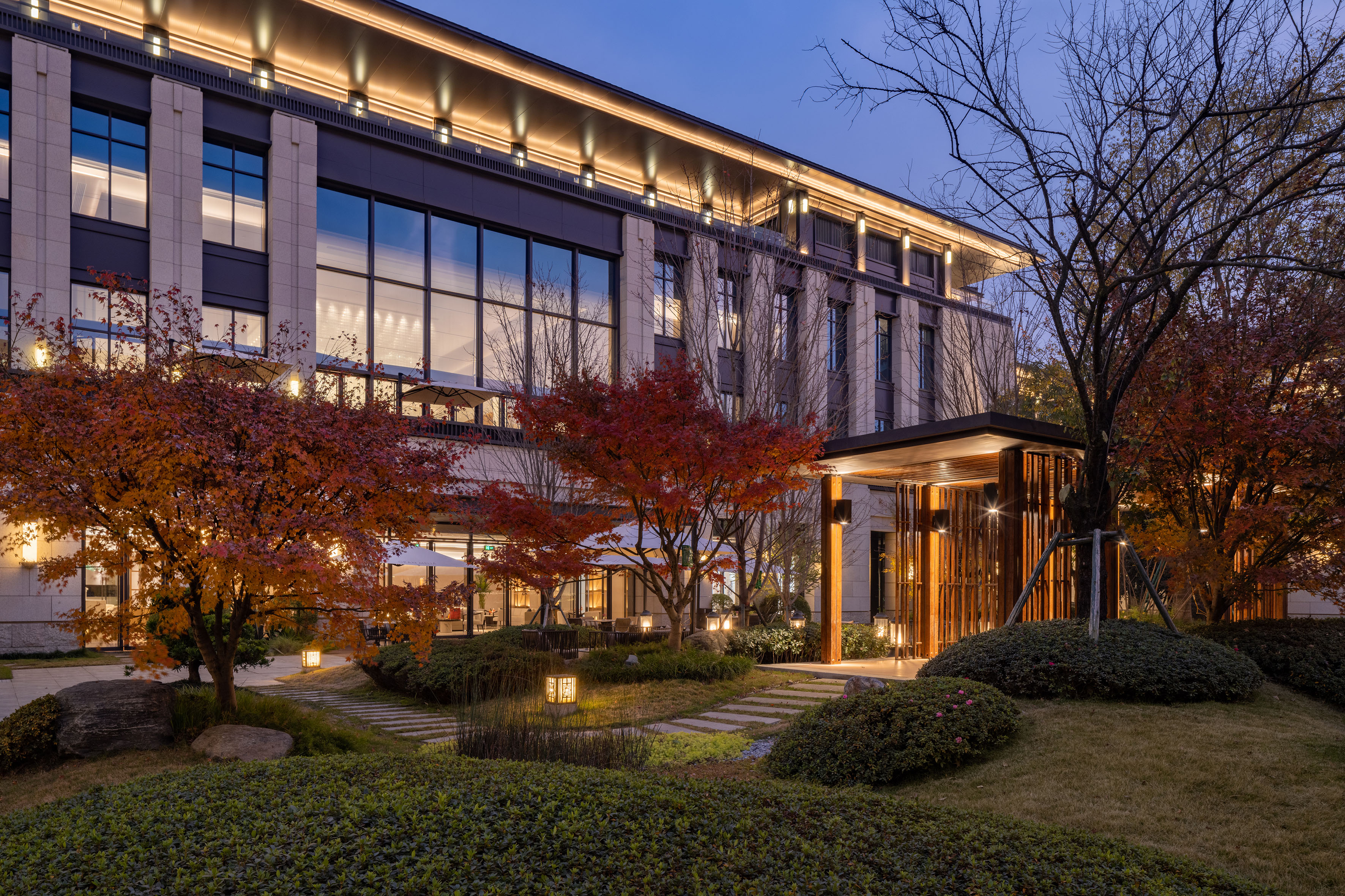 Illuminated modern building, autumn trees, and elegant garden path at dusk.