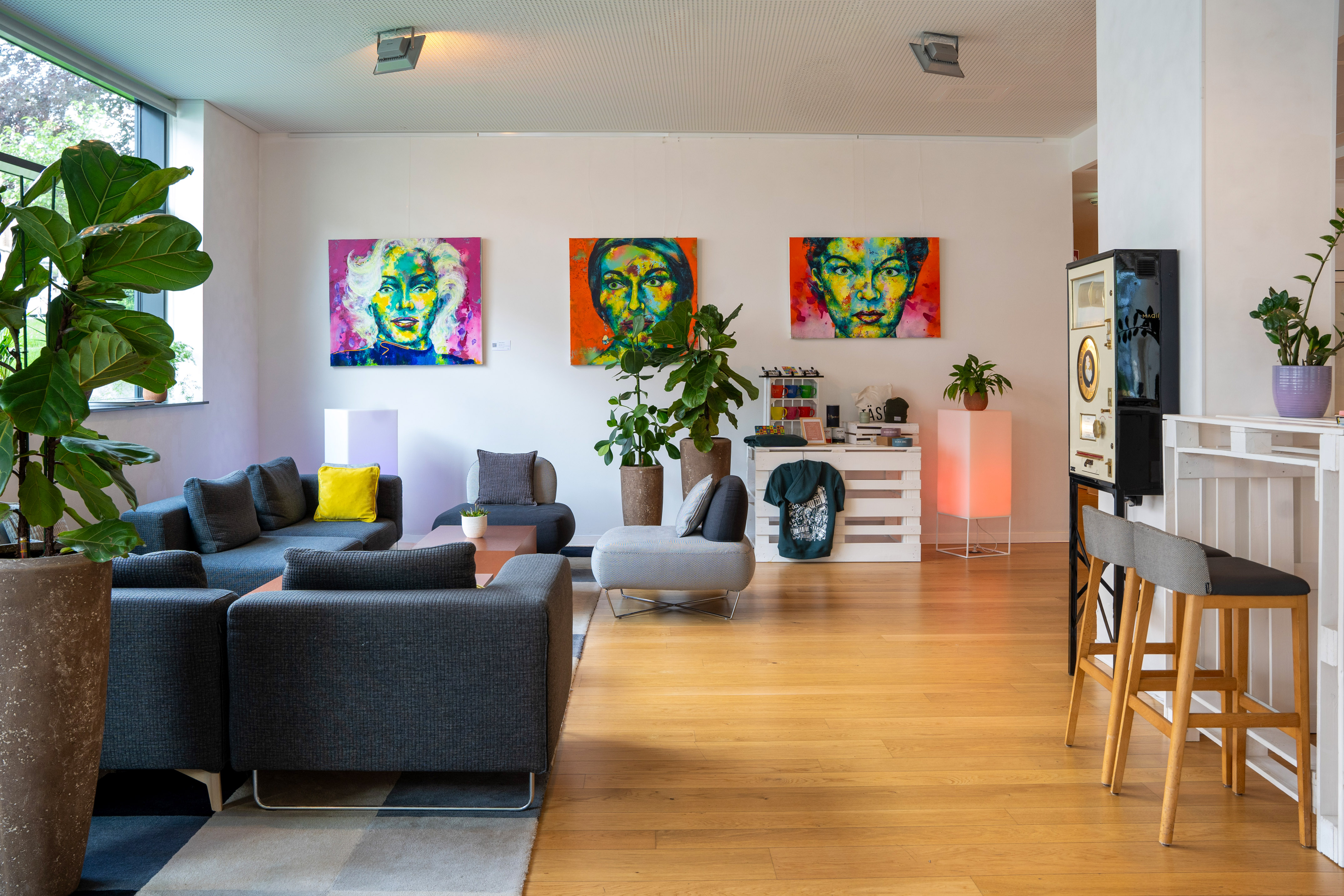 Vibrant modern lounge with pop art portraits, grey sofas, and potted plants.