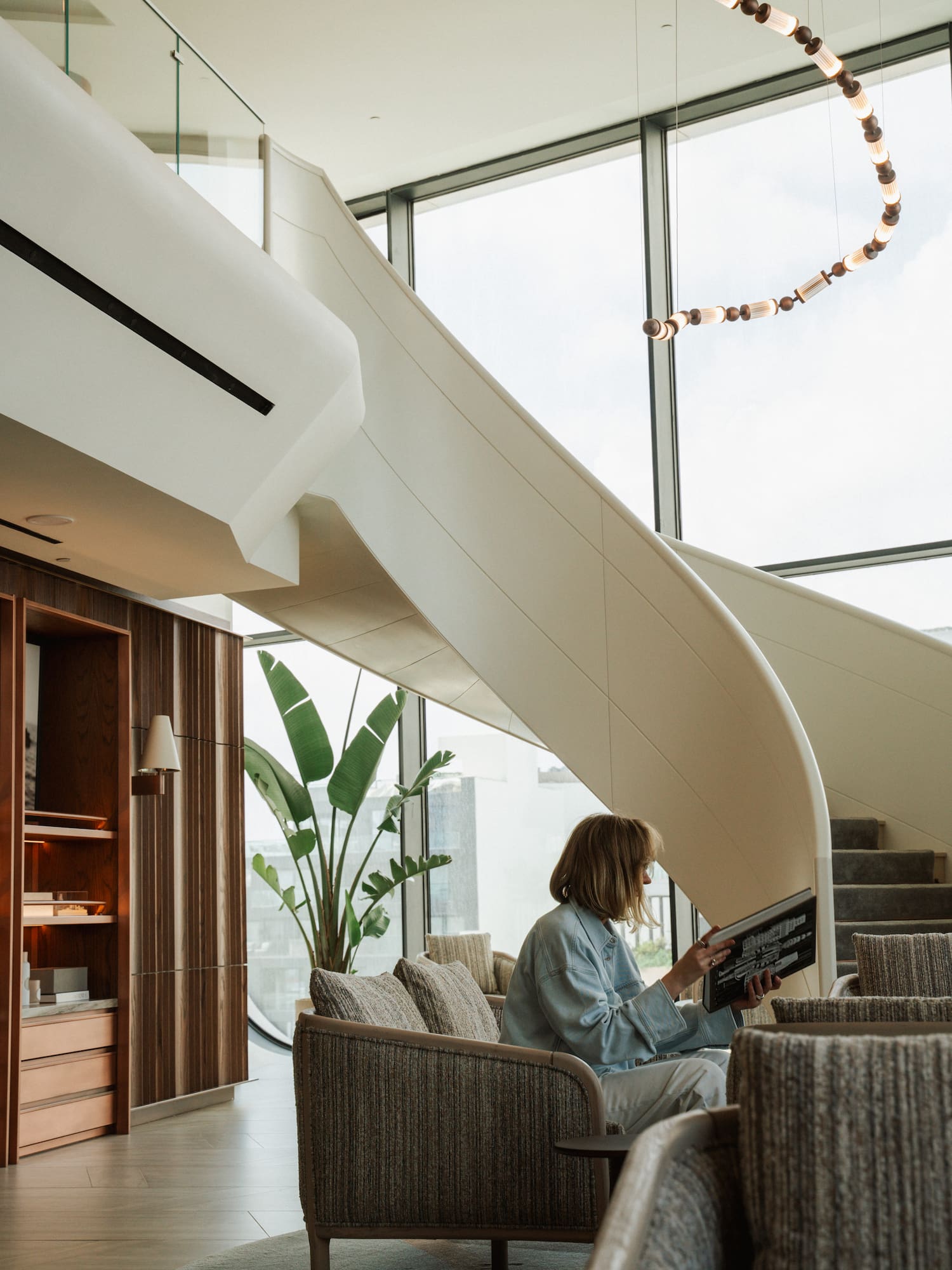 Woman reading in bright modern lounge with spiral staircase and windows.