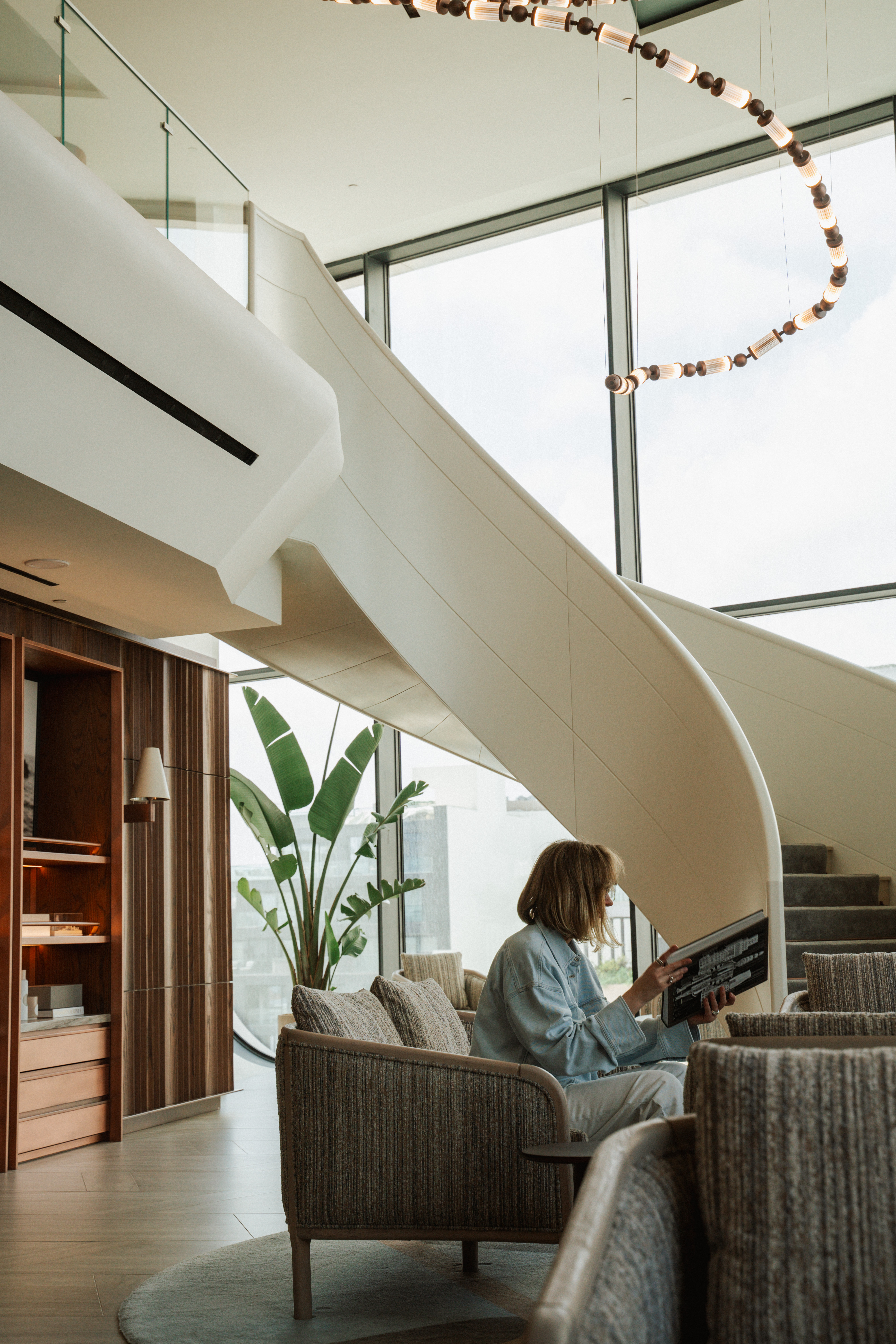 Woman reading in bright modern lounge with spiral staircase and windows.