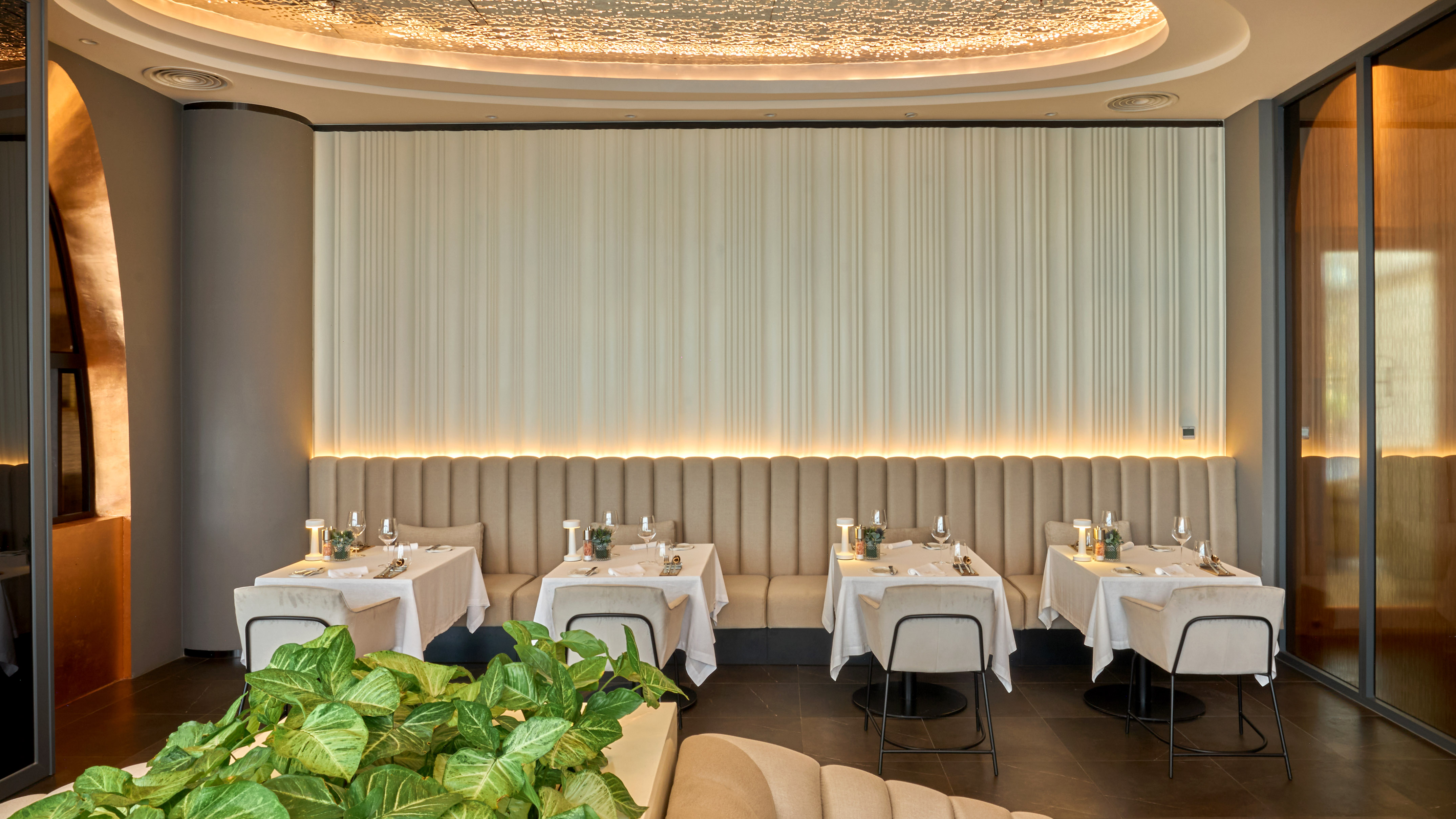 Elegant restaurant dining room with banquette seating, set tables, and warm lighting.