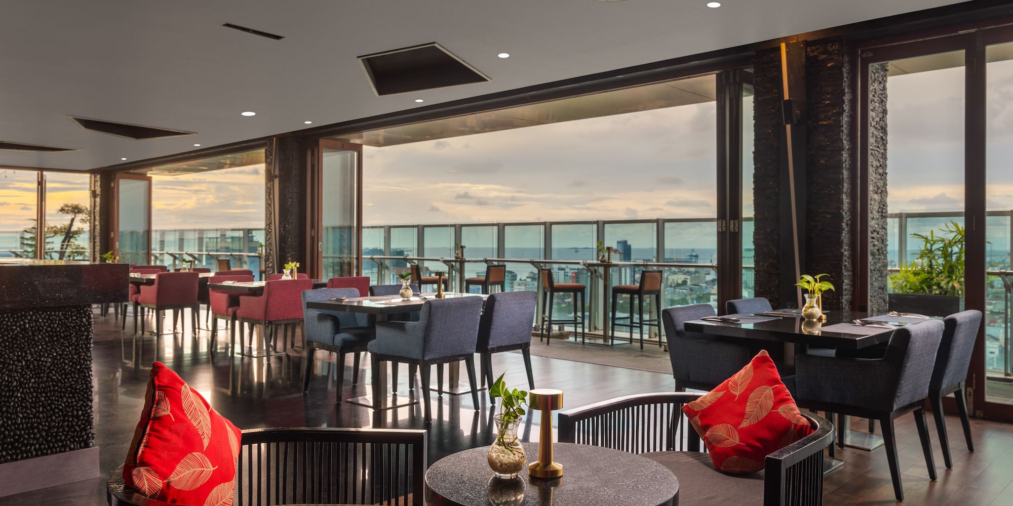 a room with tables and chairs and a balcony overlooking the water