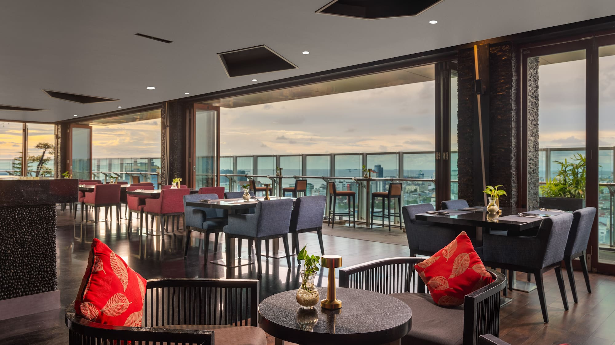 a room with tables and chairs and a balcony overlooking the water