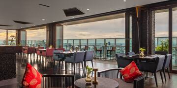 a room with tables and chairs and a balcony overlooking the water