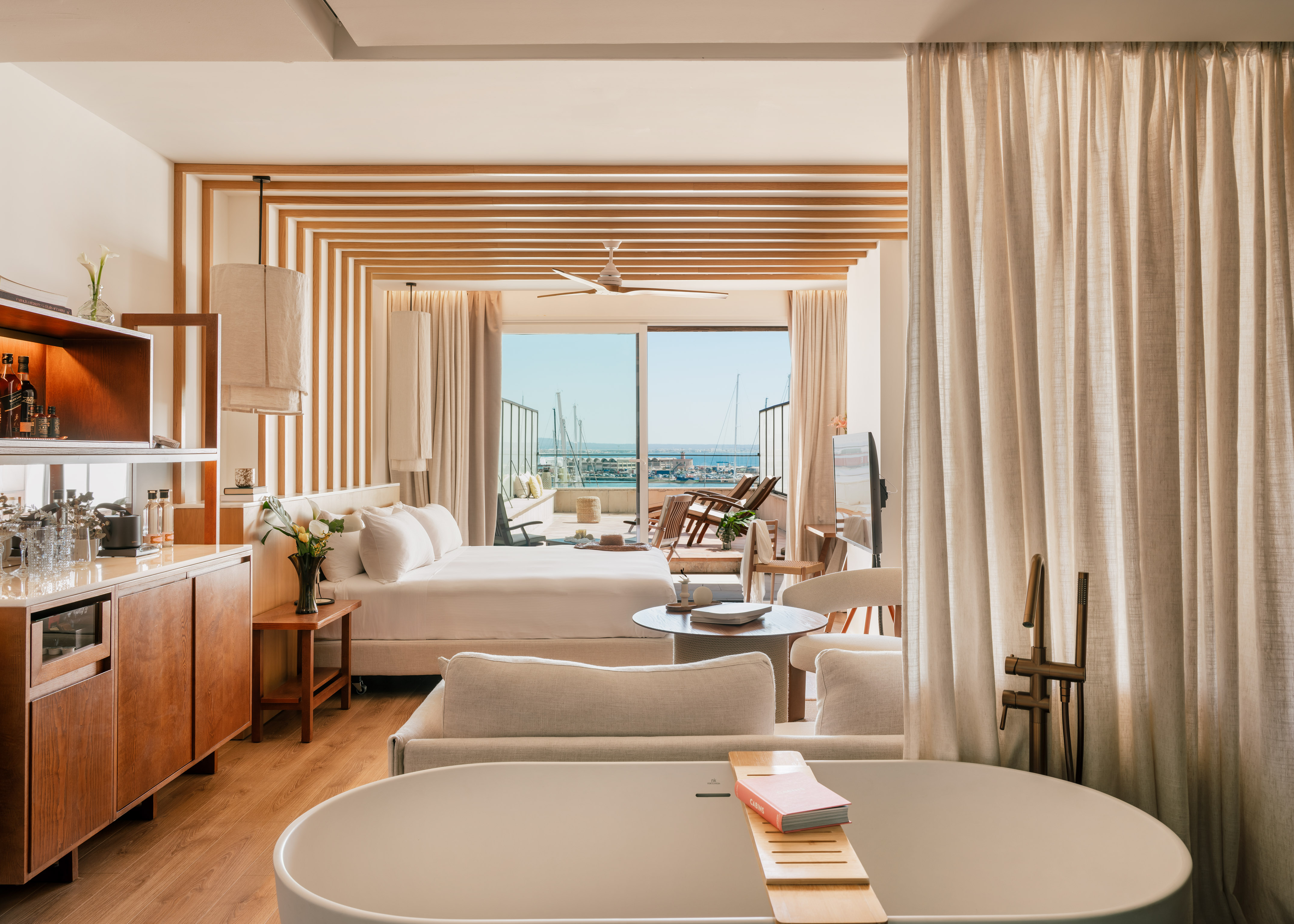 Elegant suite with marina view, king bed, balcony, and freestanding tub.