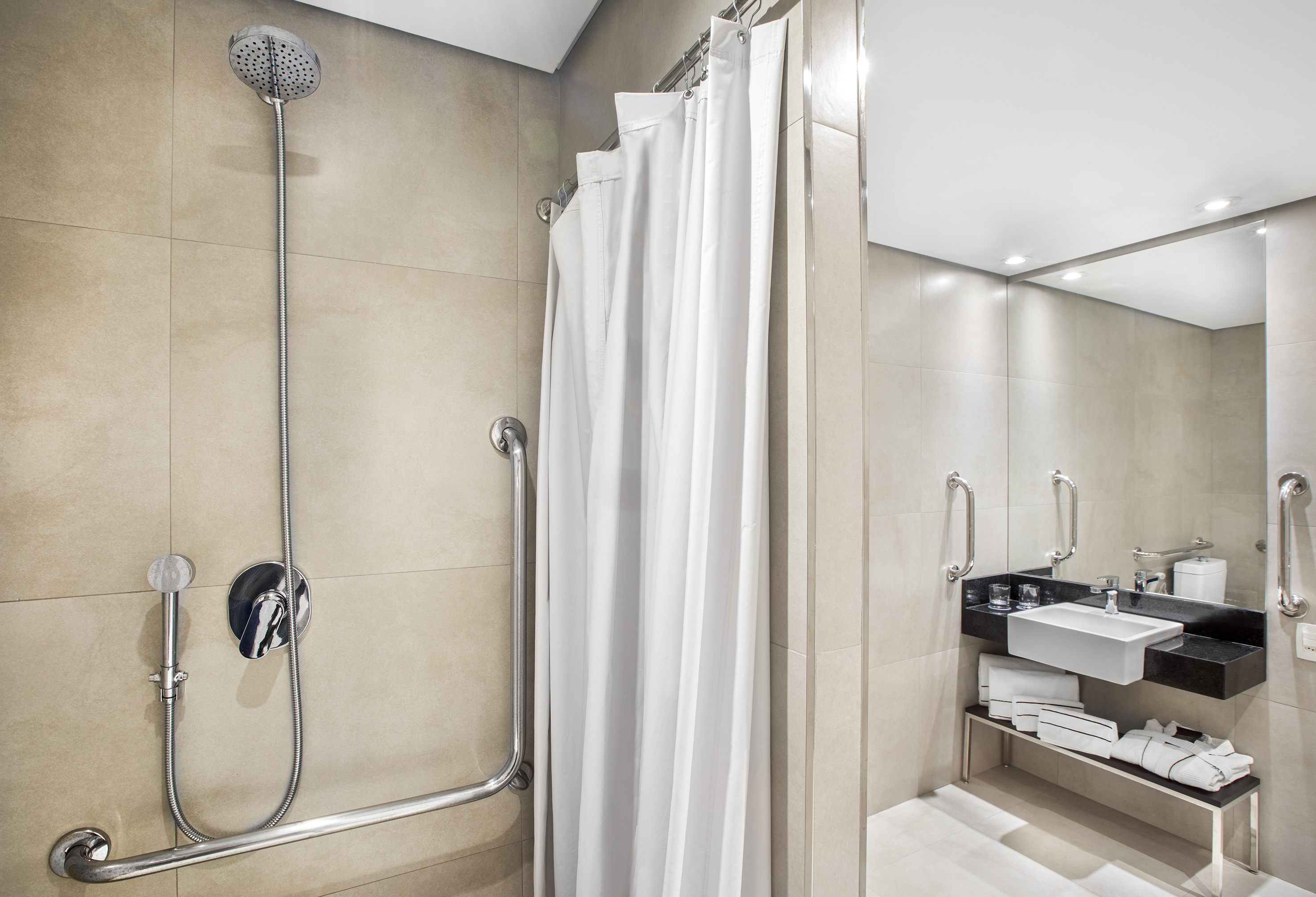 Modern accessible bathroom with shower, grab bars, white curtain, and sink.