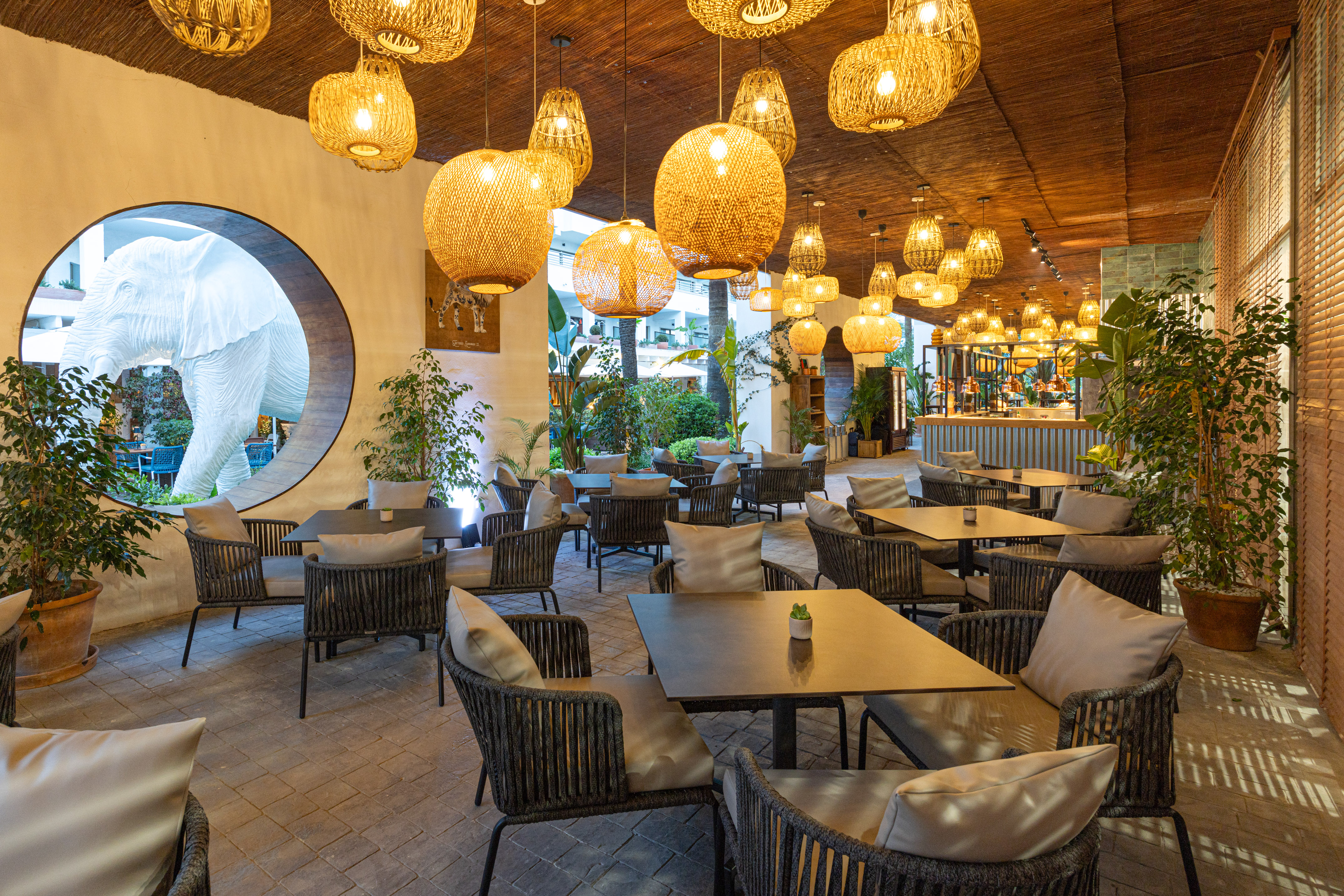 Restaurant with rattan lights, cozy seating, and a large white elephant sculpture.