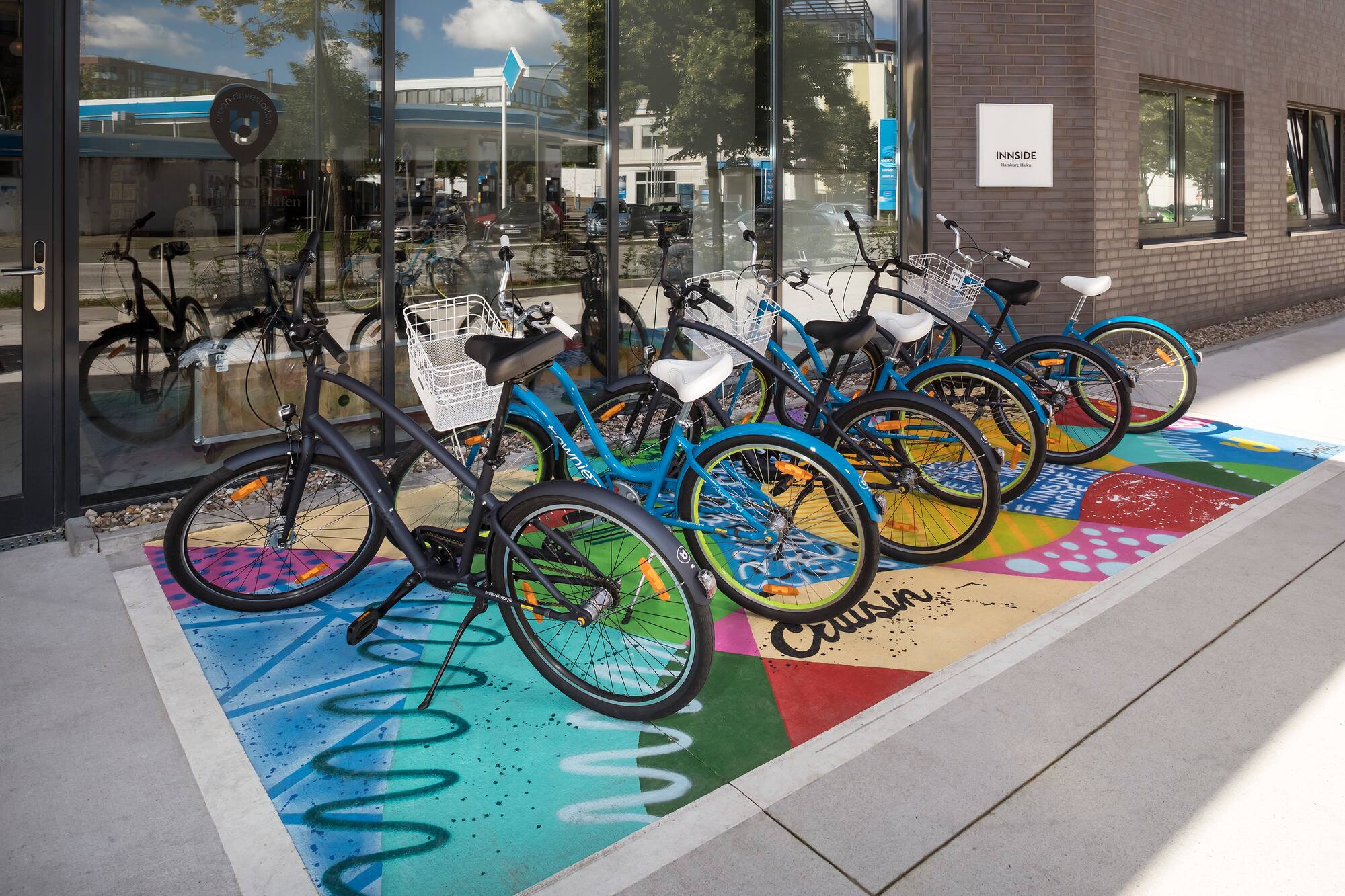 Blue and black bikes on colorful ground outside INNSIDE Hamburg Hafen.
