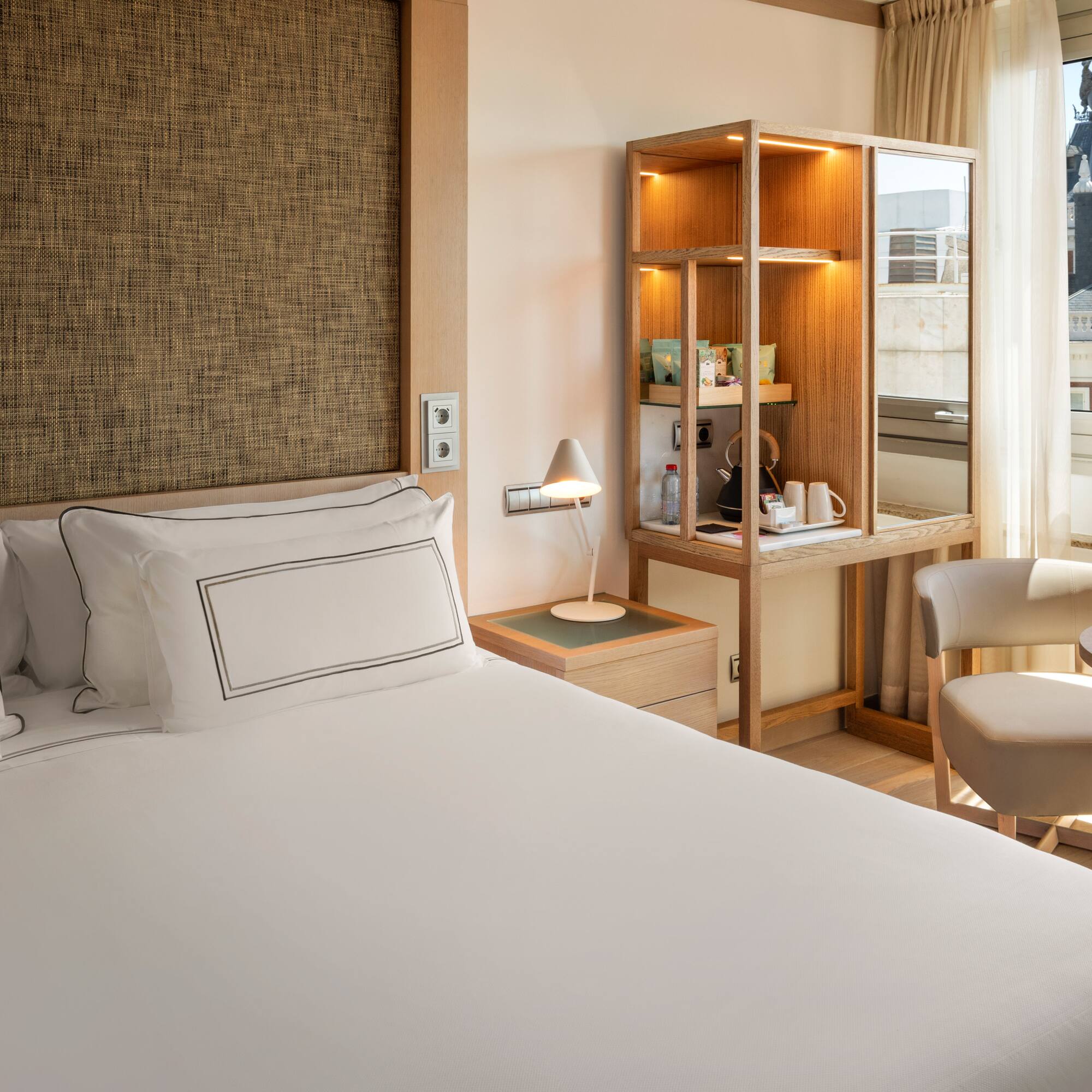 a bed with a white cover and a chair in a room with a window