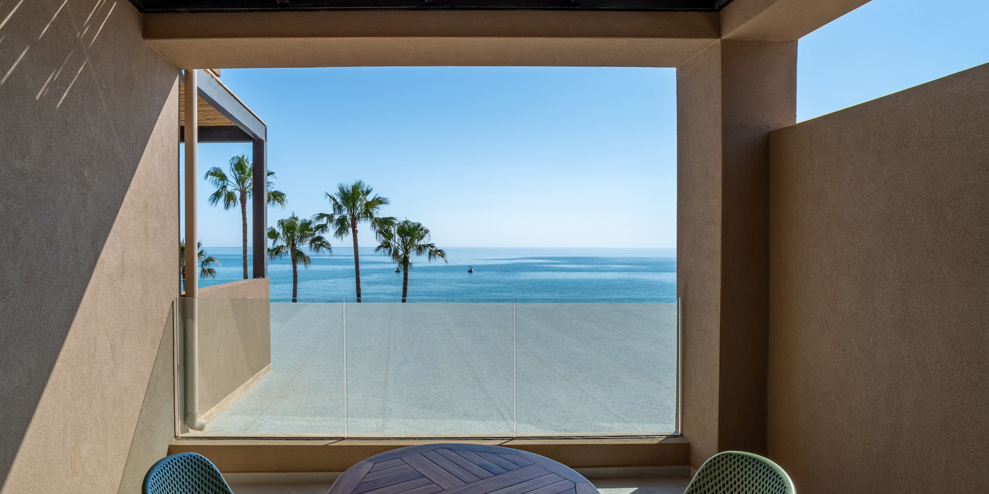 Modern balcony with ocean view, palm trees, and outdoor table.