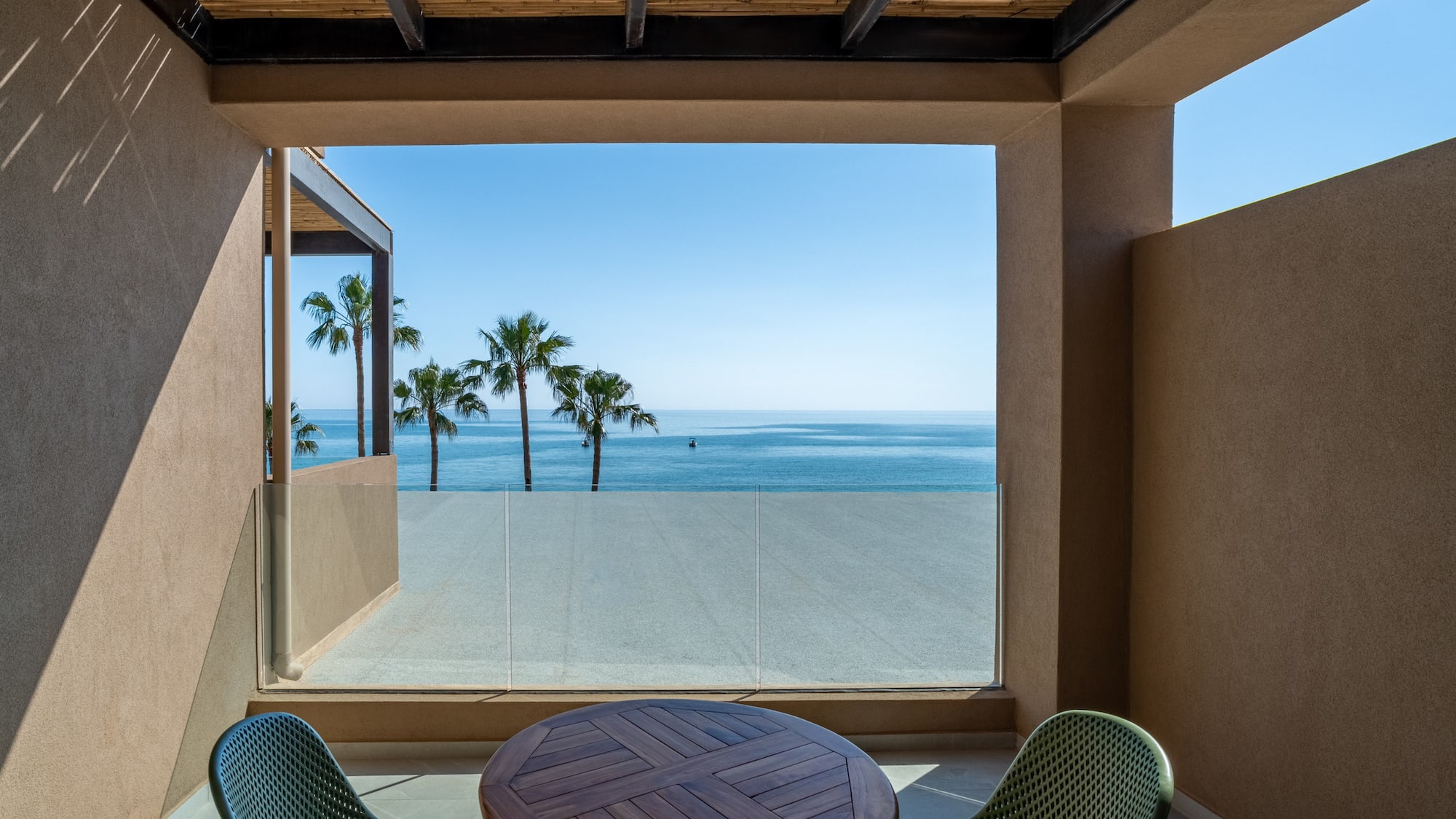 Modern balcony with ocean view, palm trees, and outdoor table.