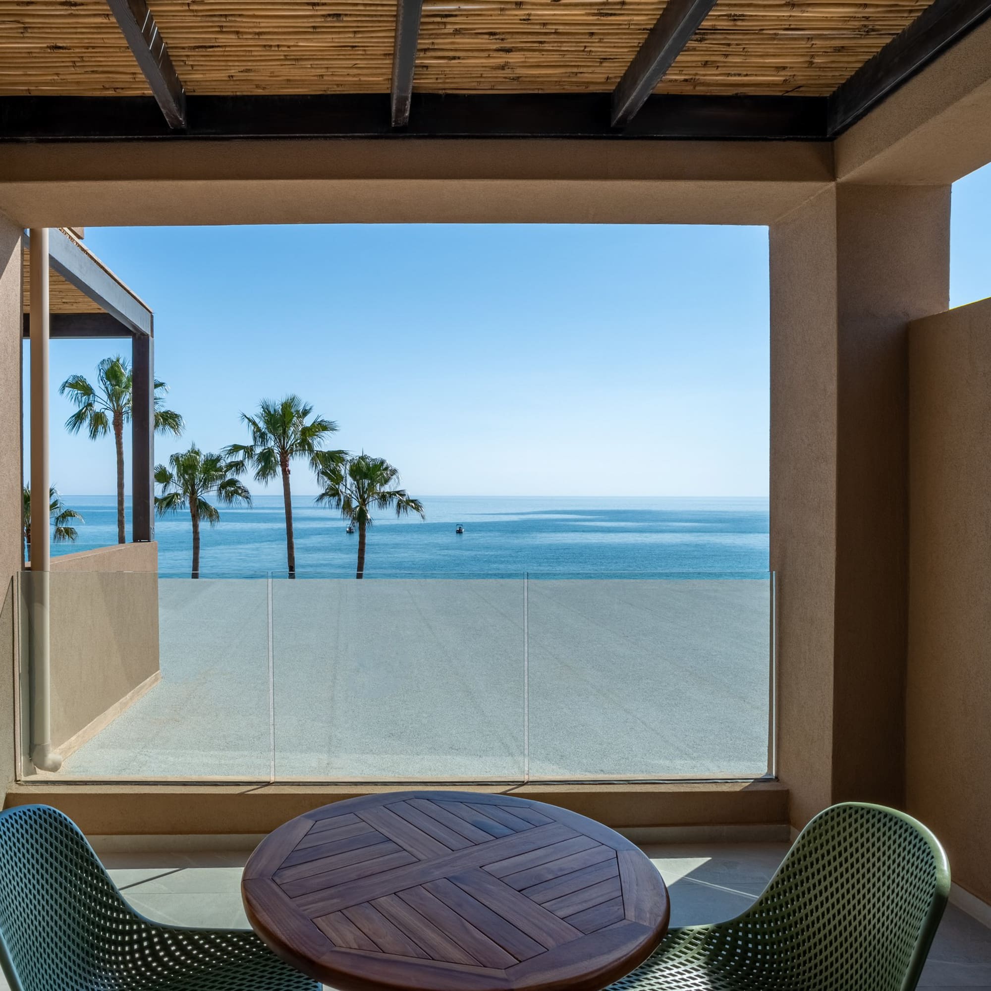Modern balcony with ocean view, palm trees, and outdoor table.