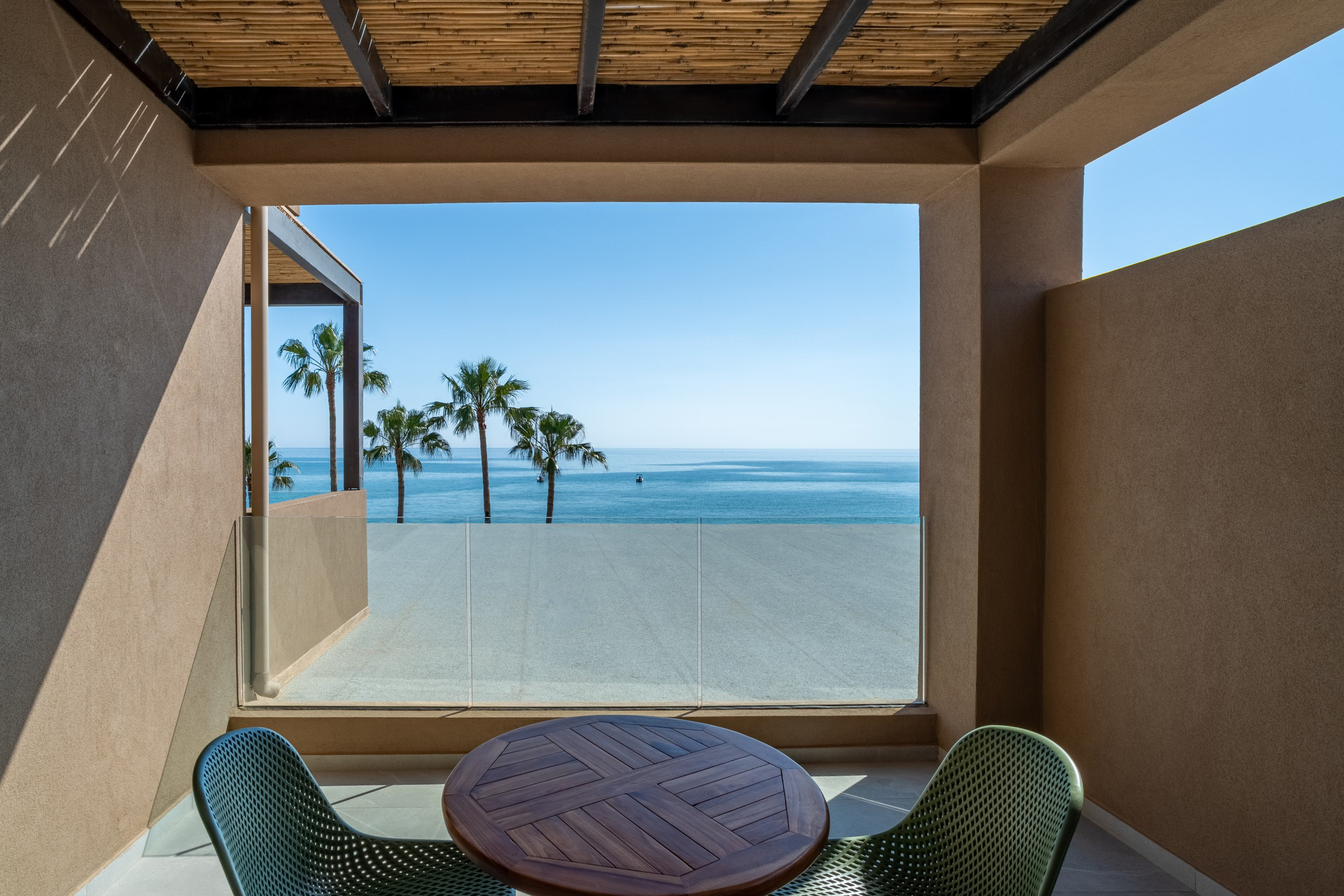 Modern balcony with ocean view, palm trees, and outdoor table.