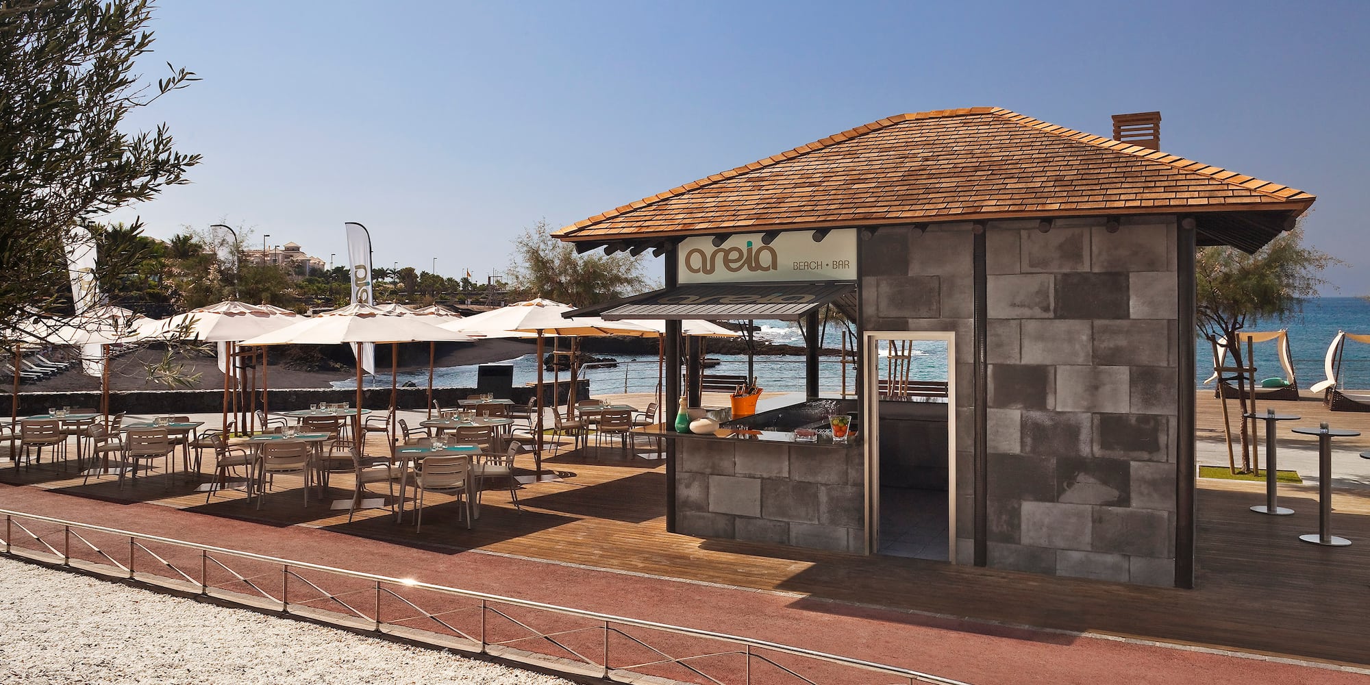 Areia Beach Bar outdoor patio with tables, umbrellas, and ocean view.