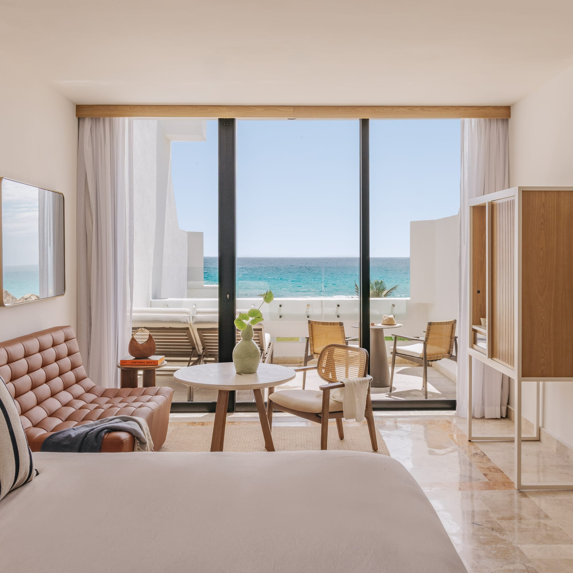 Modern hotel suite with ocean view balcony, leather sofa, and rattan accents.