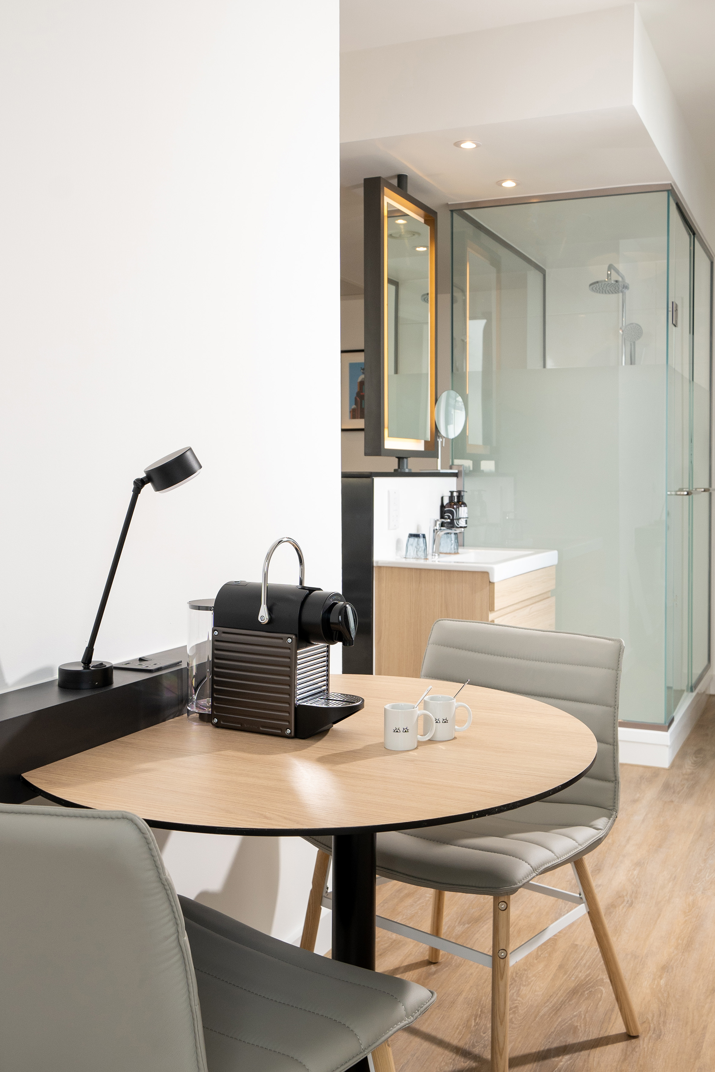 Modern room with Nespresso machine, round table, chairs, and glass shower.