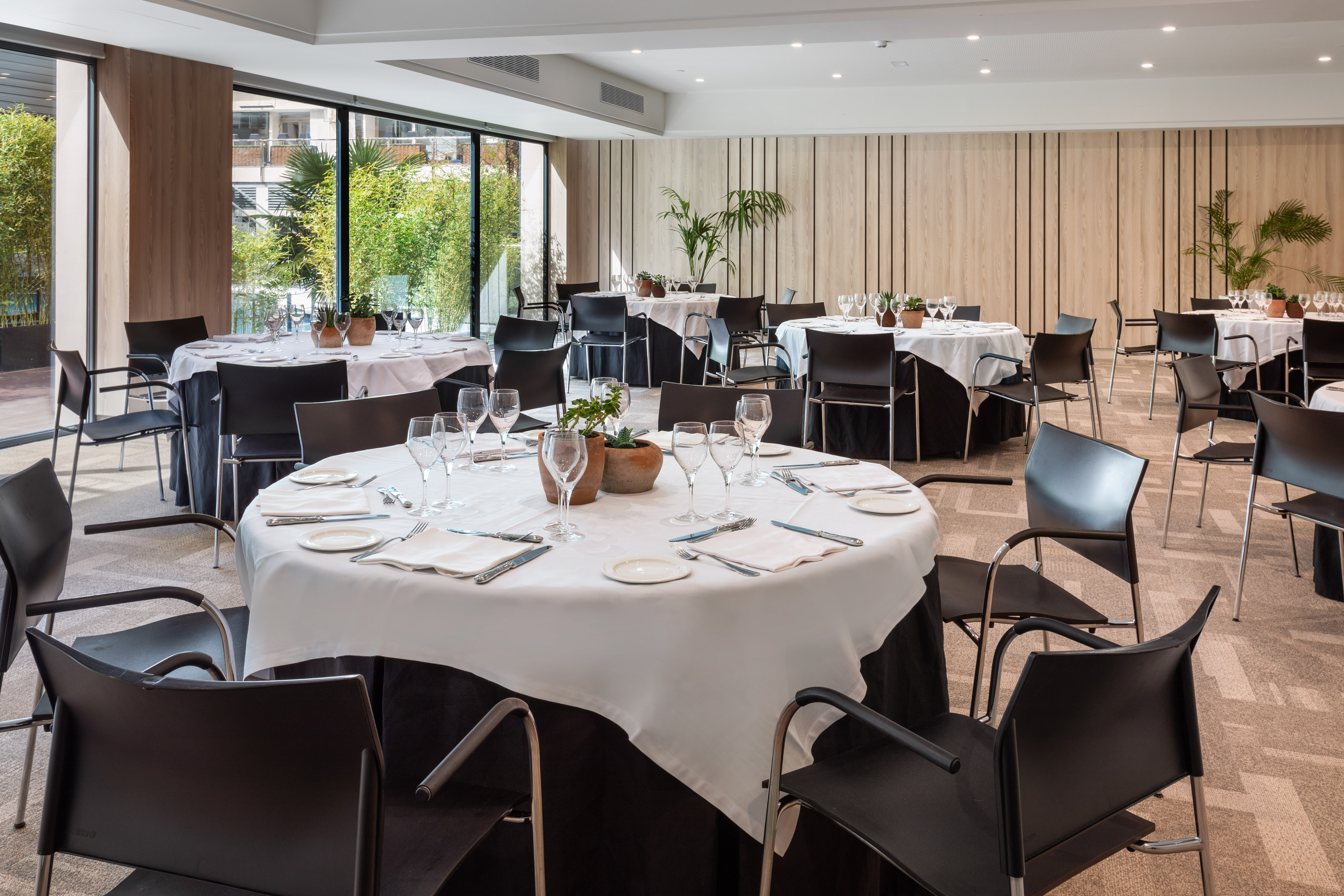 Modern restaurant dining room with set tables, black chairs, and natural light.