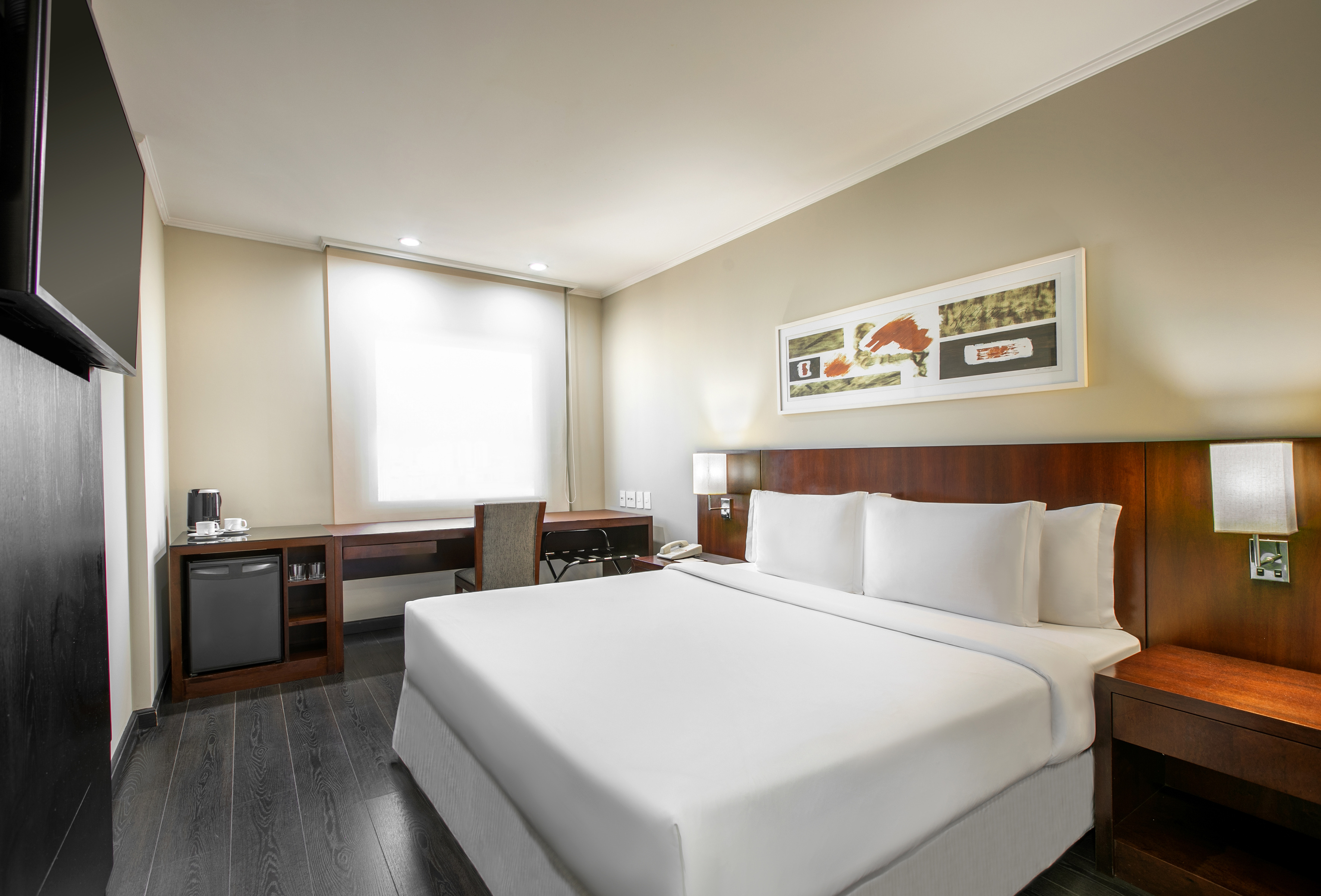 Modern hotel guest room with queen bed, desk, mini-fridge, and TV.