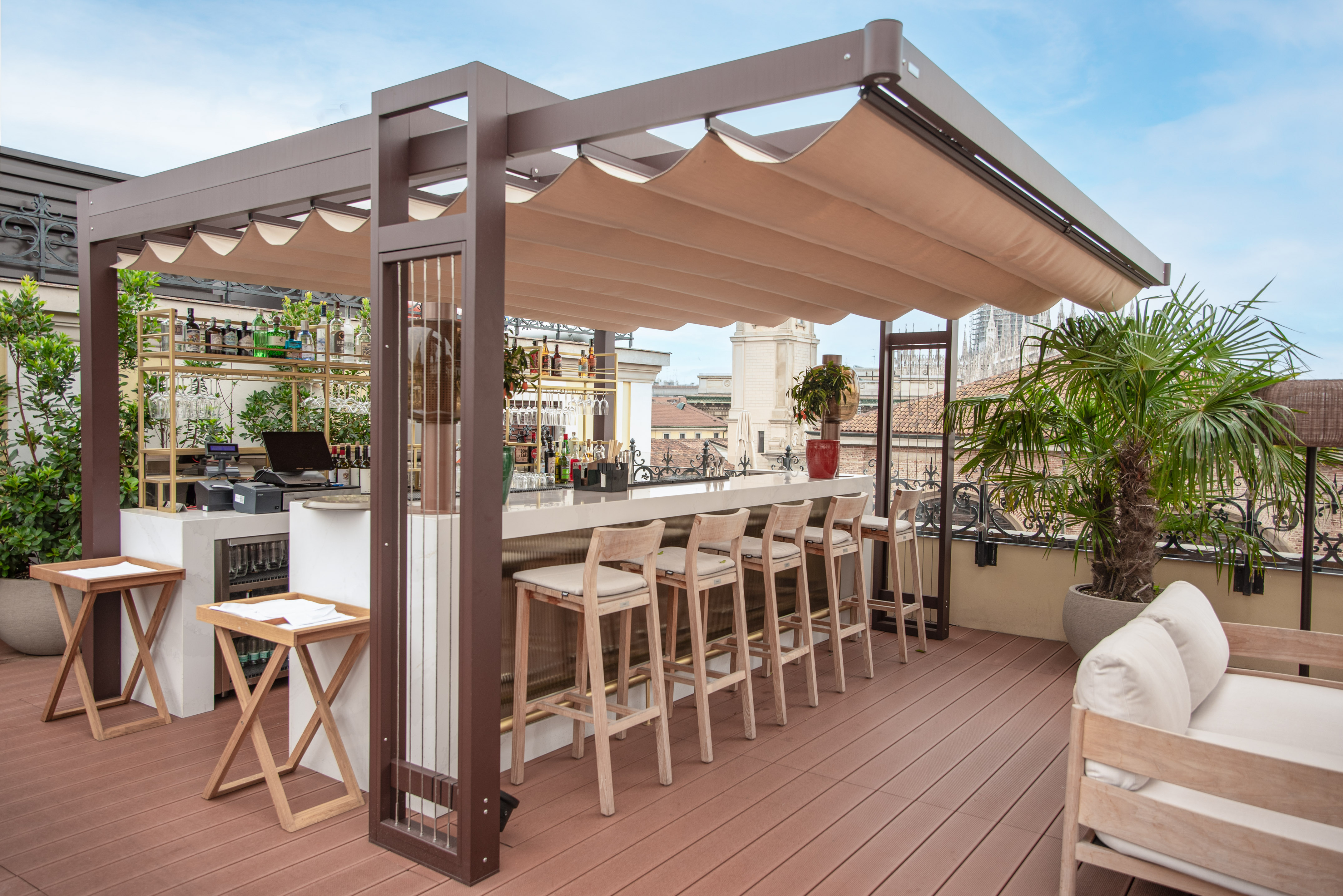 Outdoor rooftop bar under retractable canopy with stools and city view.