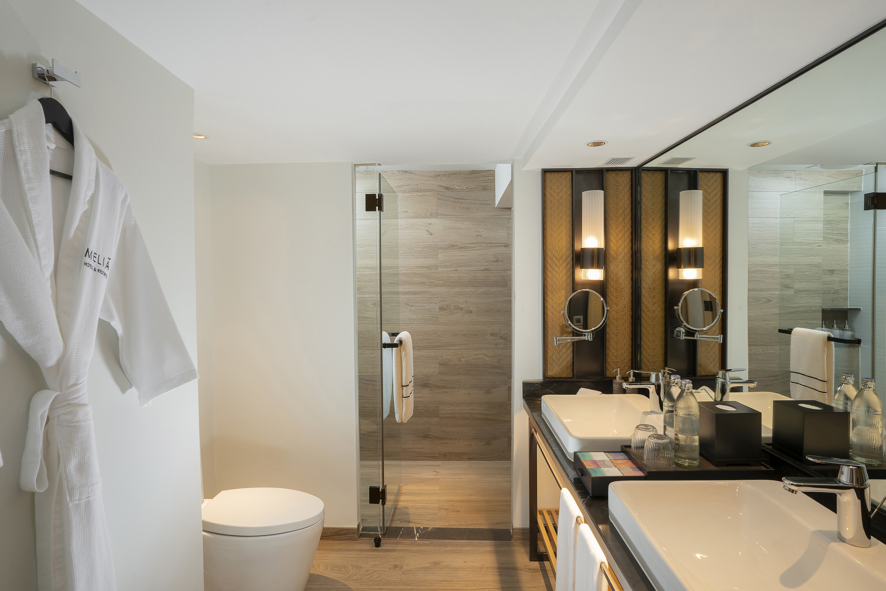 Luxury hotel bathroom with double vanity, walk-in shower, and white bathrobe.