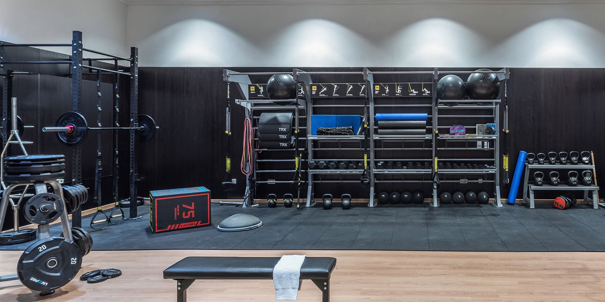 Modern gym with squat rack, weight bench, kettlebells, dumbbells, and exercise gear.