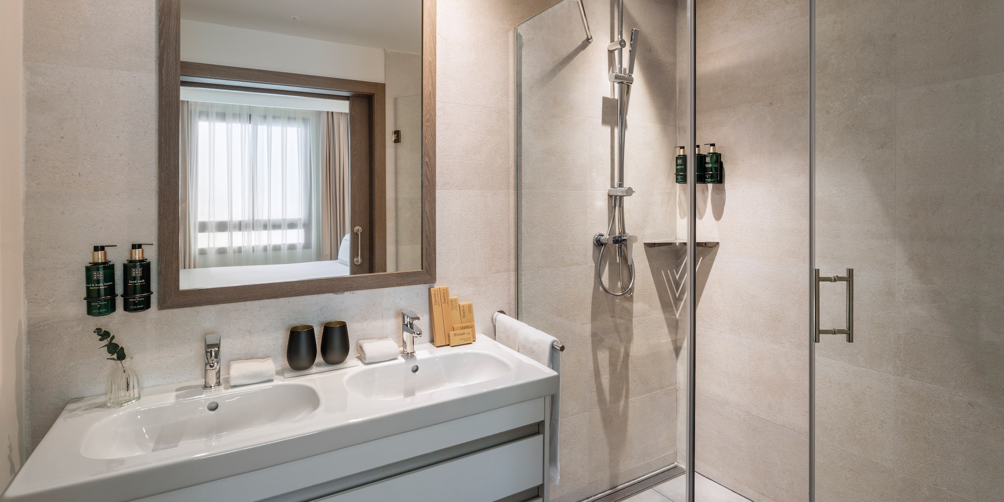 Modern hotel bathroom with double vanity, mirror, and glass shower.