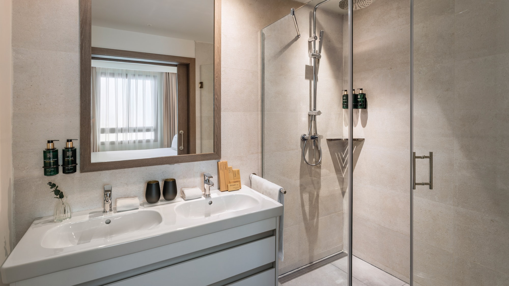 Modern hotel bathroom with double vanity, mirror, and glass shower.