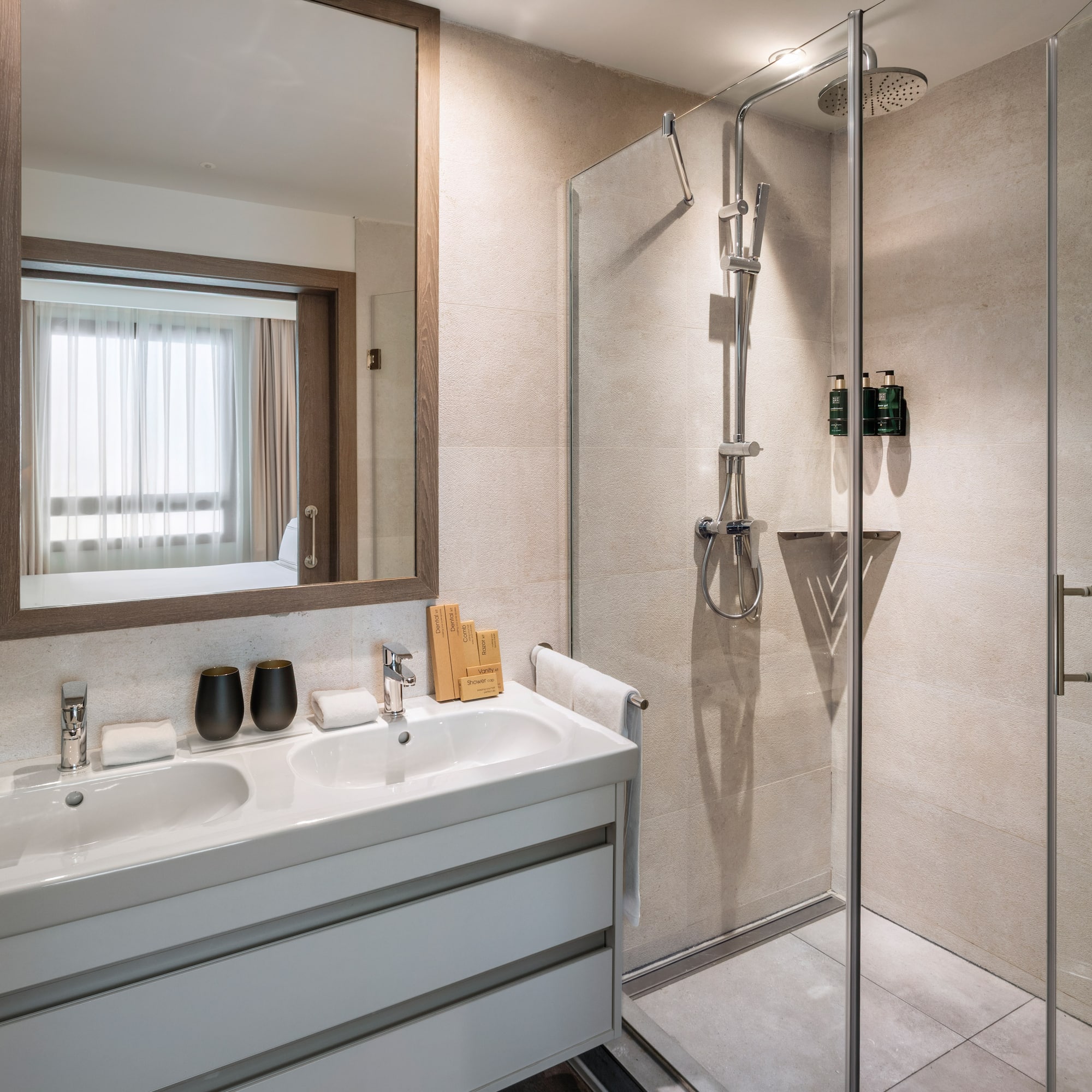 Modern hotel bathroom with double vanity, mirror, and glass shower.