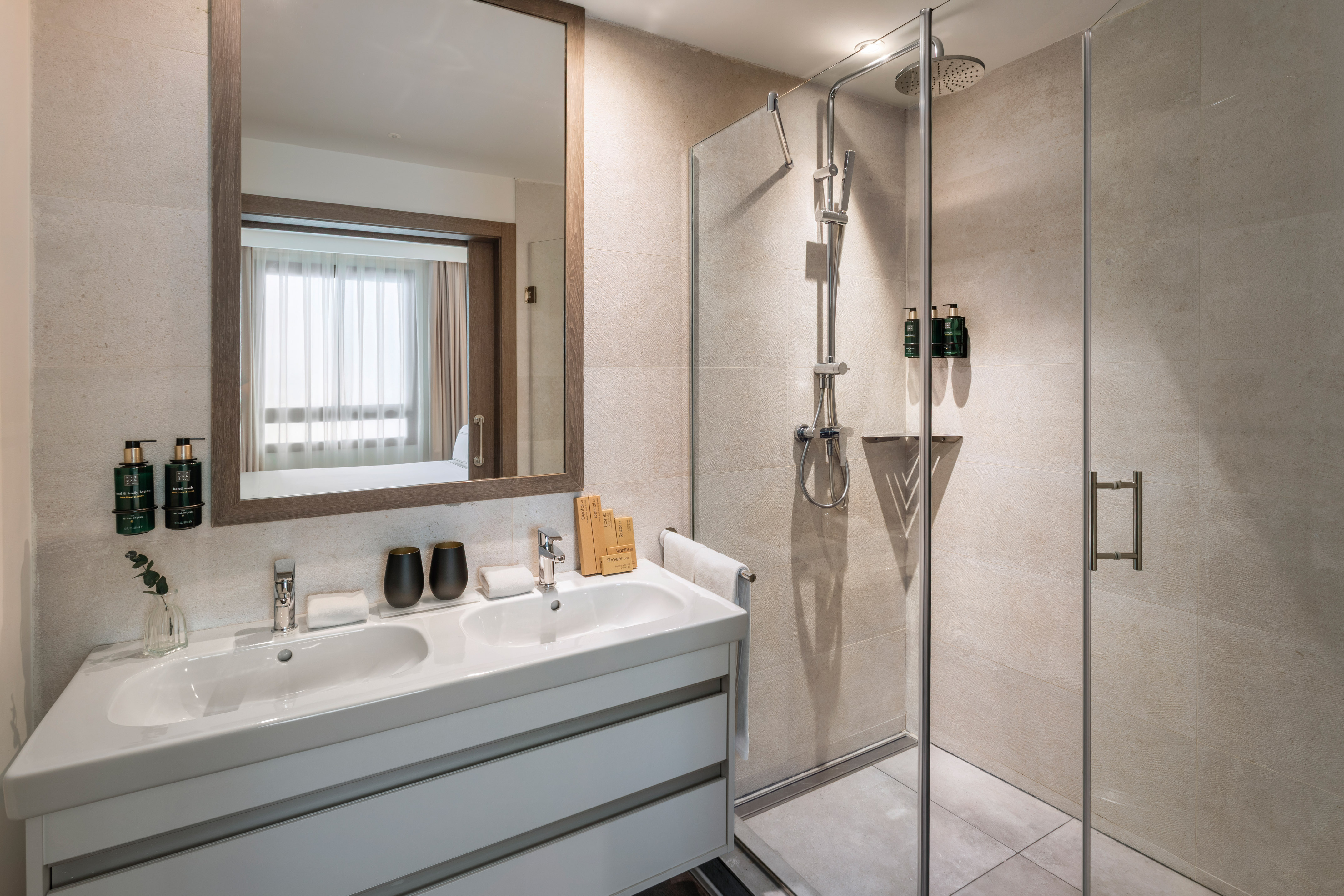 Modern hotel bathroom with double vanity, mirror, and glass shower.