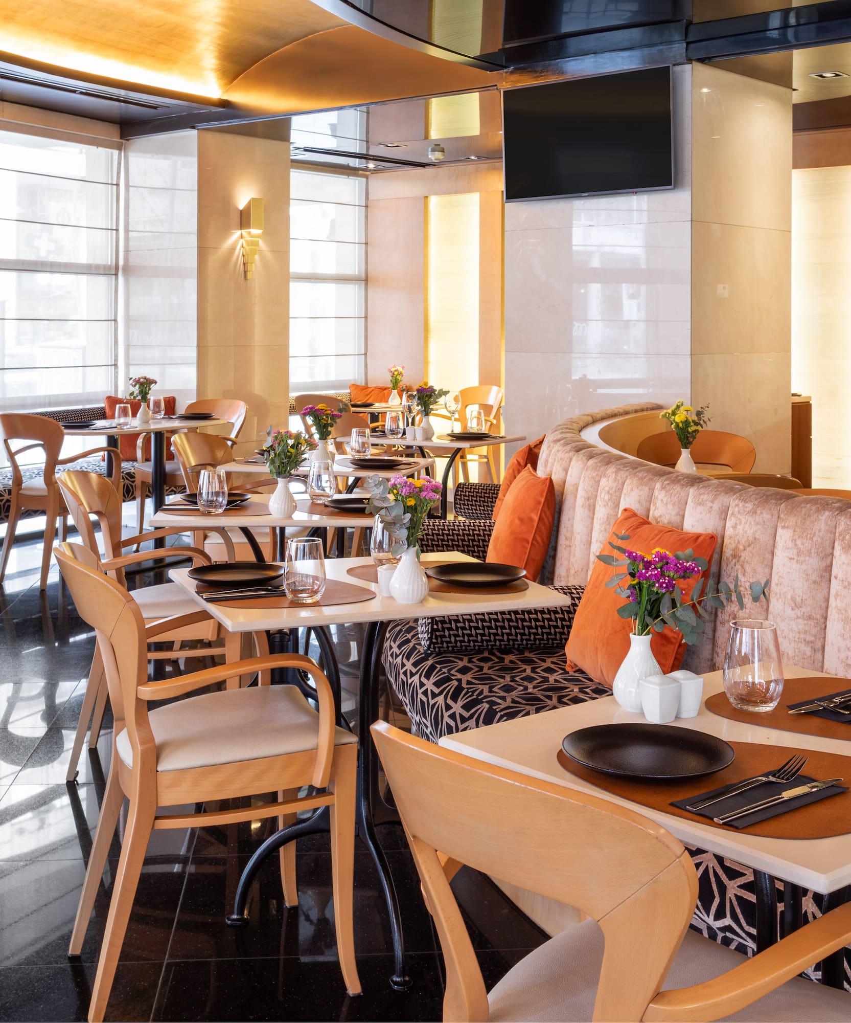 Hotel restaurant dining room with set tables, velvet booths, and warm decor.