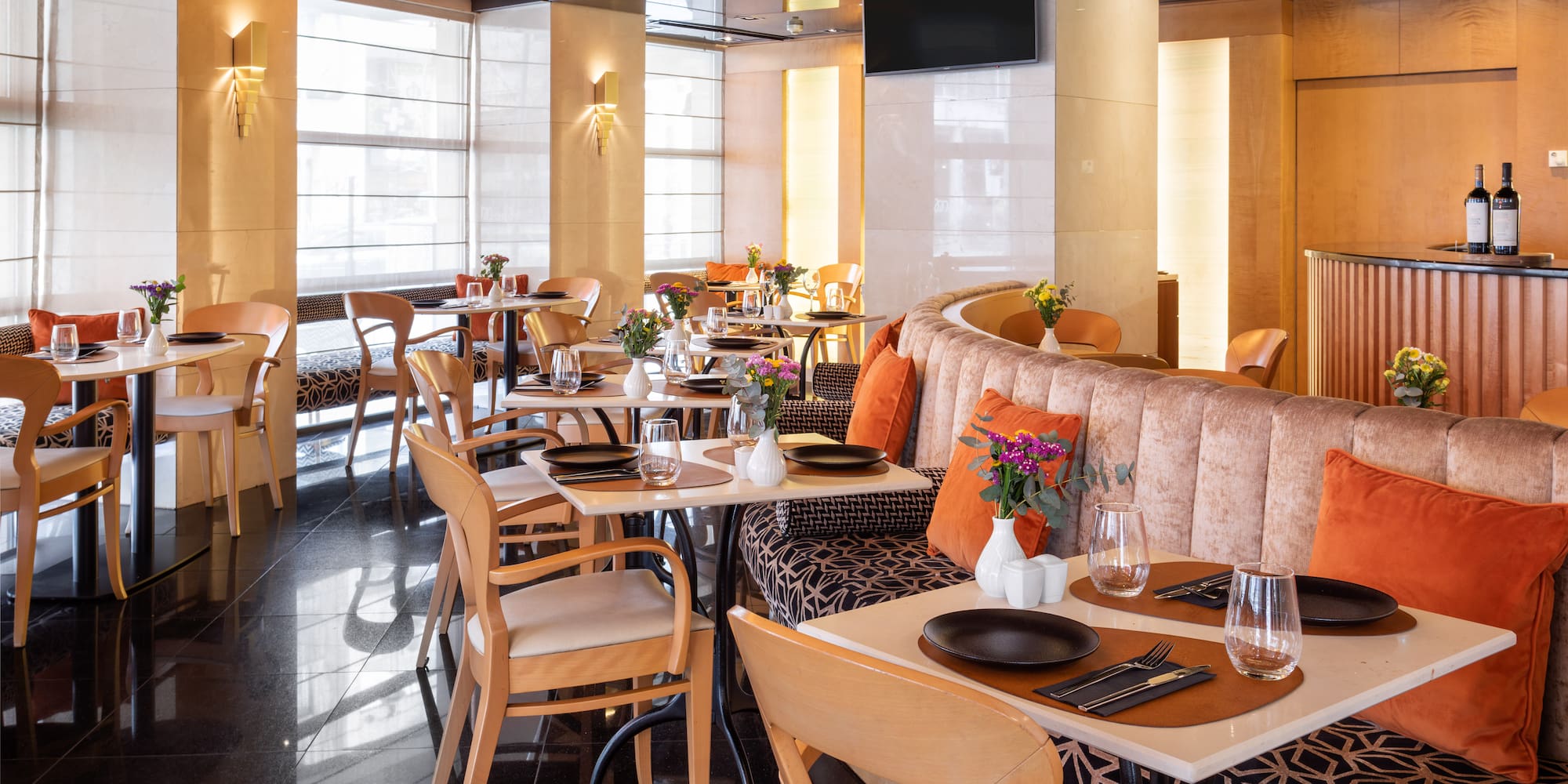 Modern restaurant dining room with set tables, banquette seating, and bright windows.