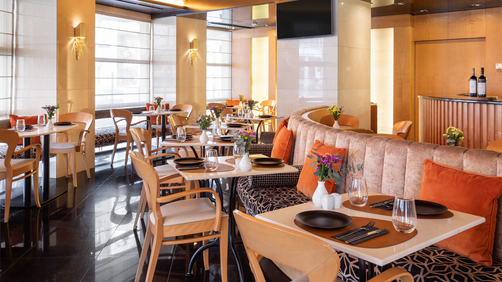 Modern restaurant dining room with set tables, banquette seating, and bright windows.
